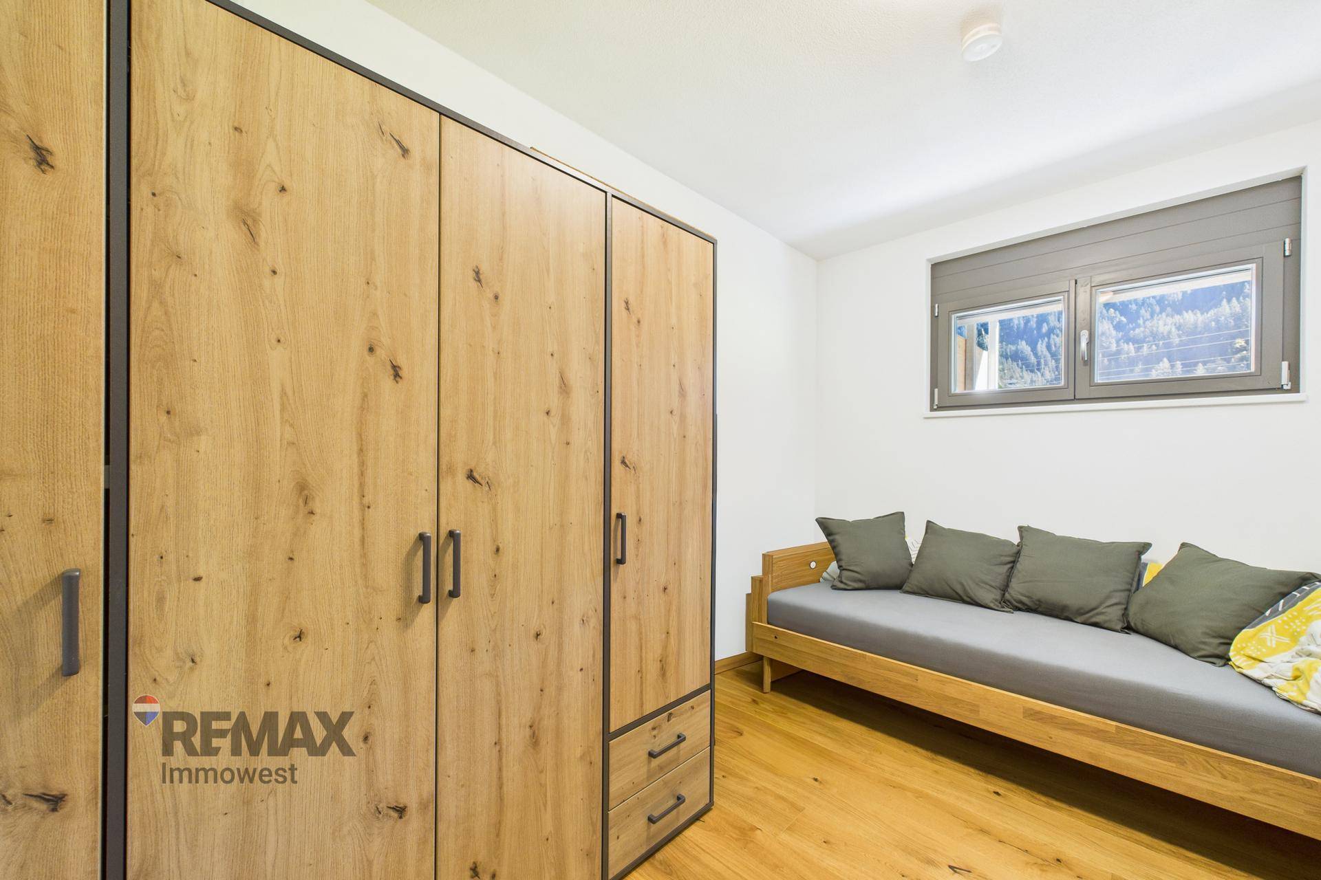 Helles Schlafzimmer mit Einzelbett, Holzschrank und Fenster mit Blick auf die Natur.