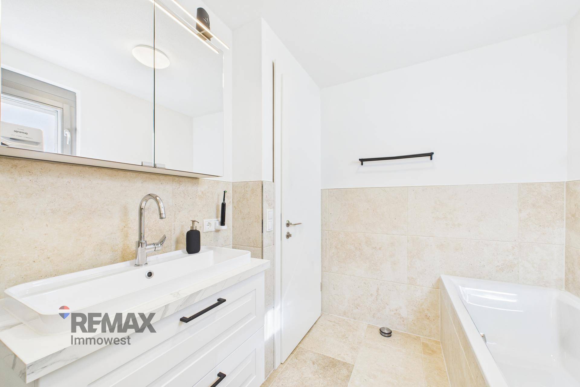 Helles Badezimmer mit Badewanne, Waschbecken und Spiegelschrank, in modernem Design gehalten.