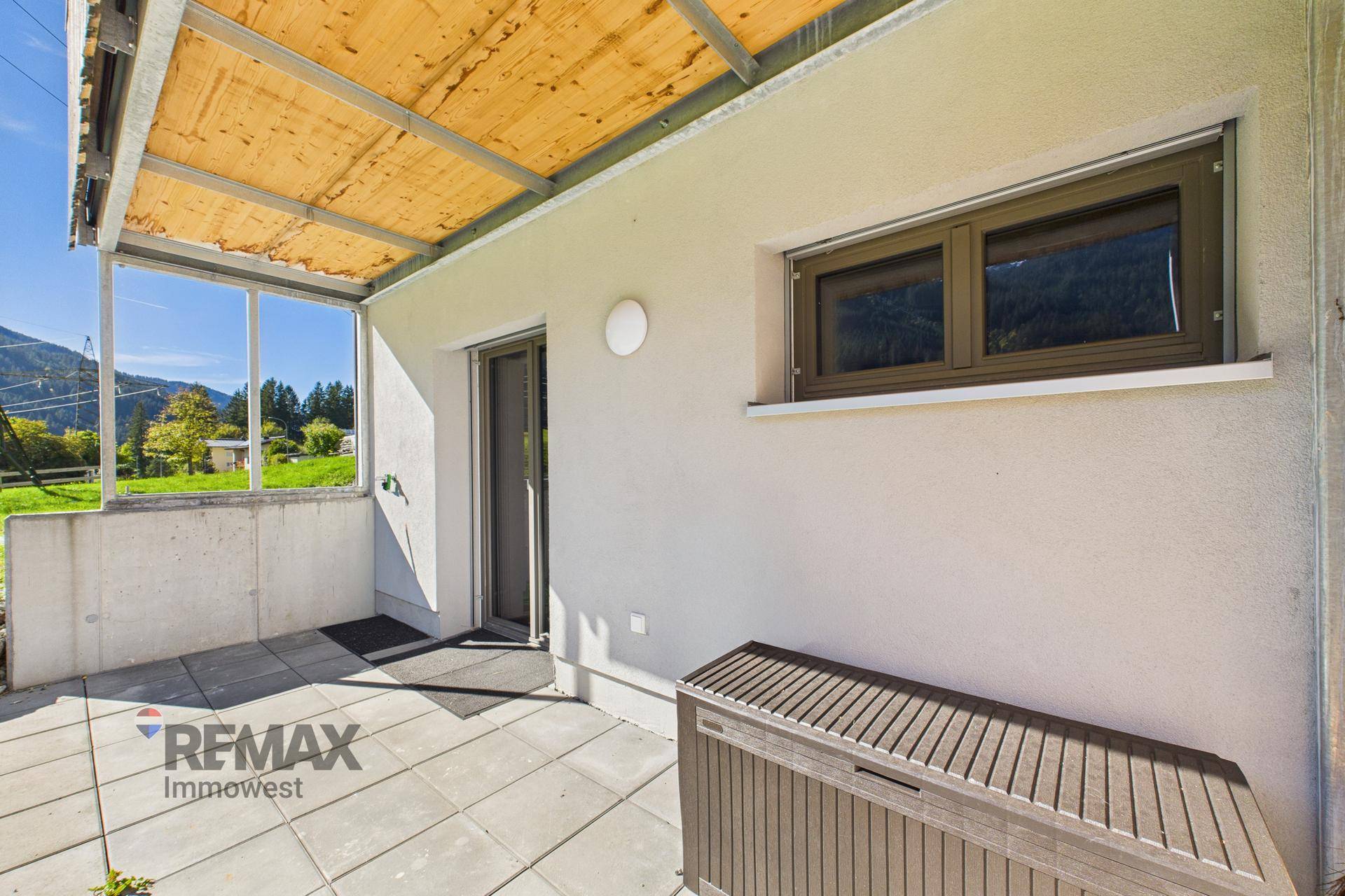Überdachte Terrasse mit Steinplatten und Stauraum, bietet direkten Zugang zum Gartenbereich.