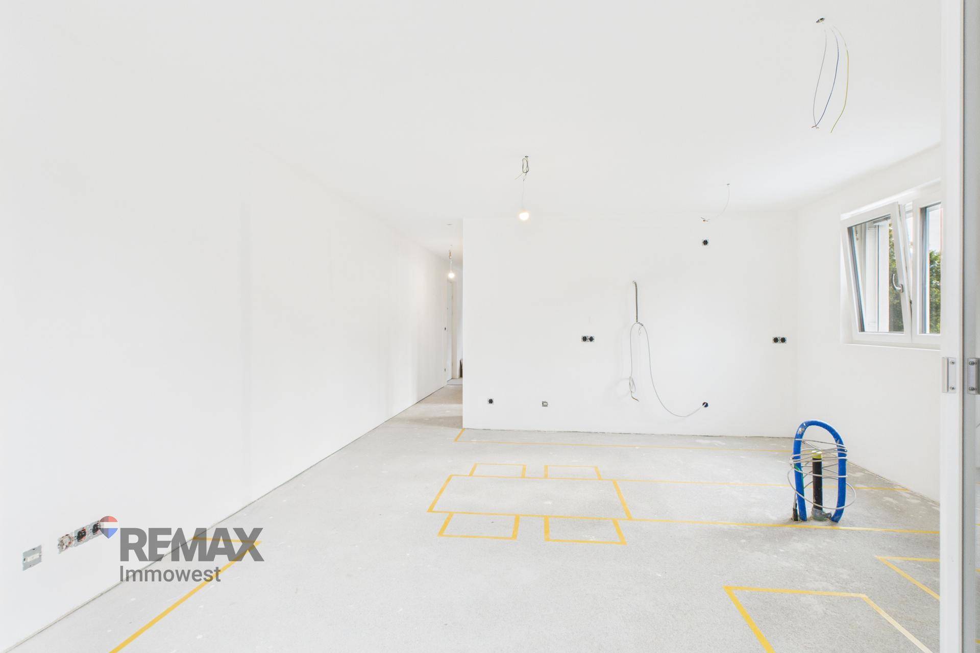 Geräumiger Rohbau-Raum mit Betonboden, weißen Wänden und Installationsvorbereitungen, hell und offen.
