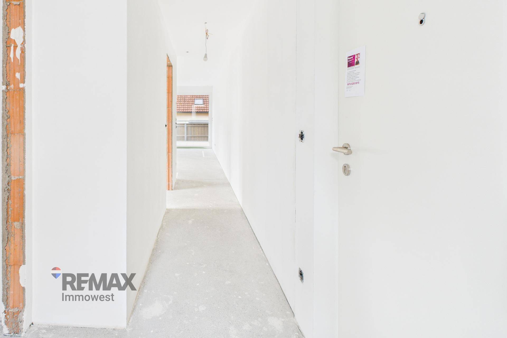 Unfertiger Flur in einem Neubau mit Rohbauwänden und Betonboden, bereit für den Innenausbau.