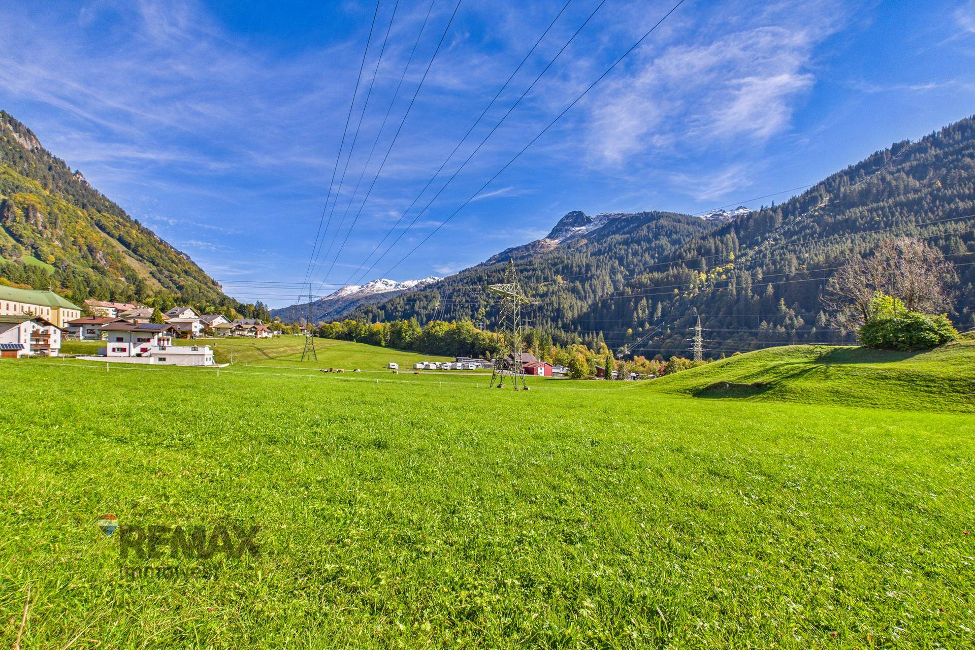 Idyllische Landschaft mit weiten grünen Wiesen und majestätischen Bergen unter blauem Himmel.