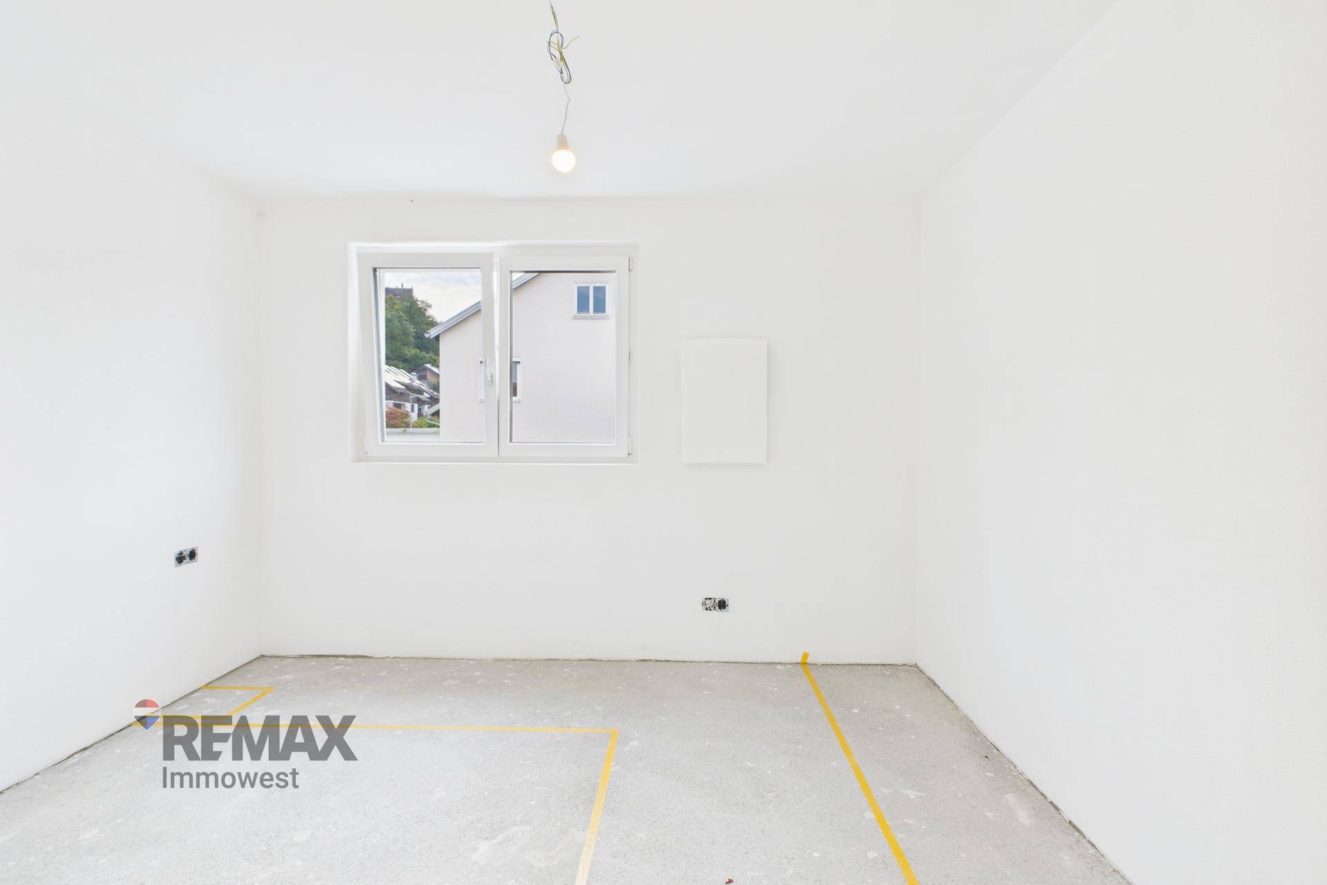Kleinerer Rohbau-Raum mit Fenster, weißen Wänden und Betonboden, bereit für den Innenausbau.