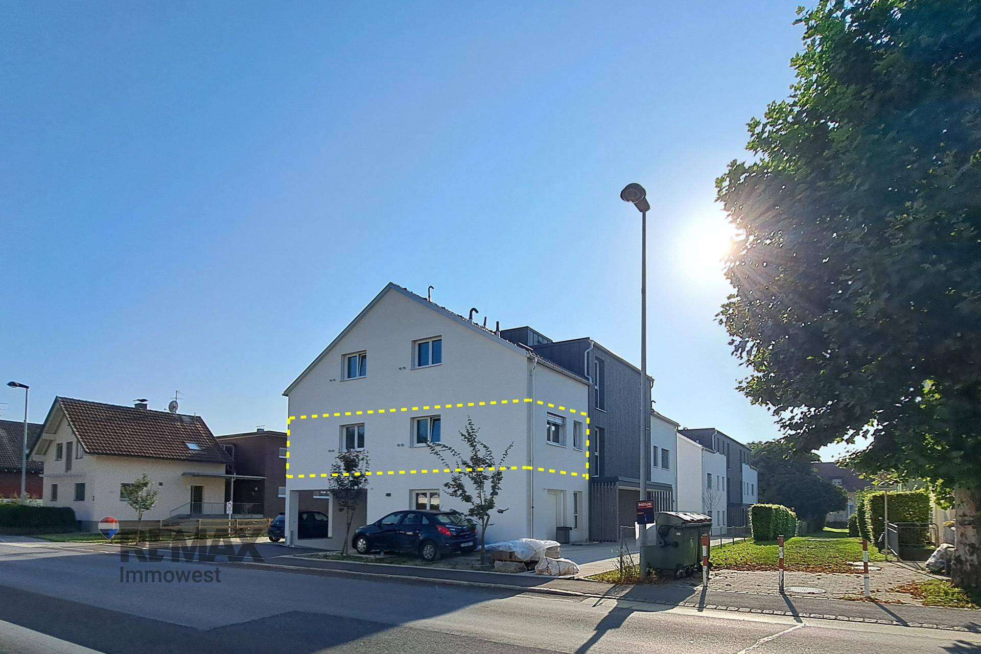 Sonnenbeschienenes Mehrfamilienhaus mit moderner Architektur, Balkonen und Parkmöglichkeiten an der Straße.