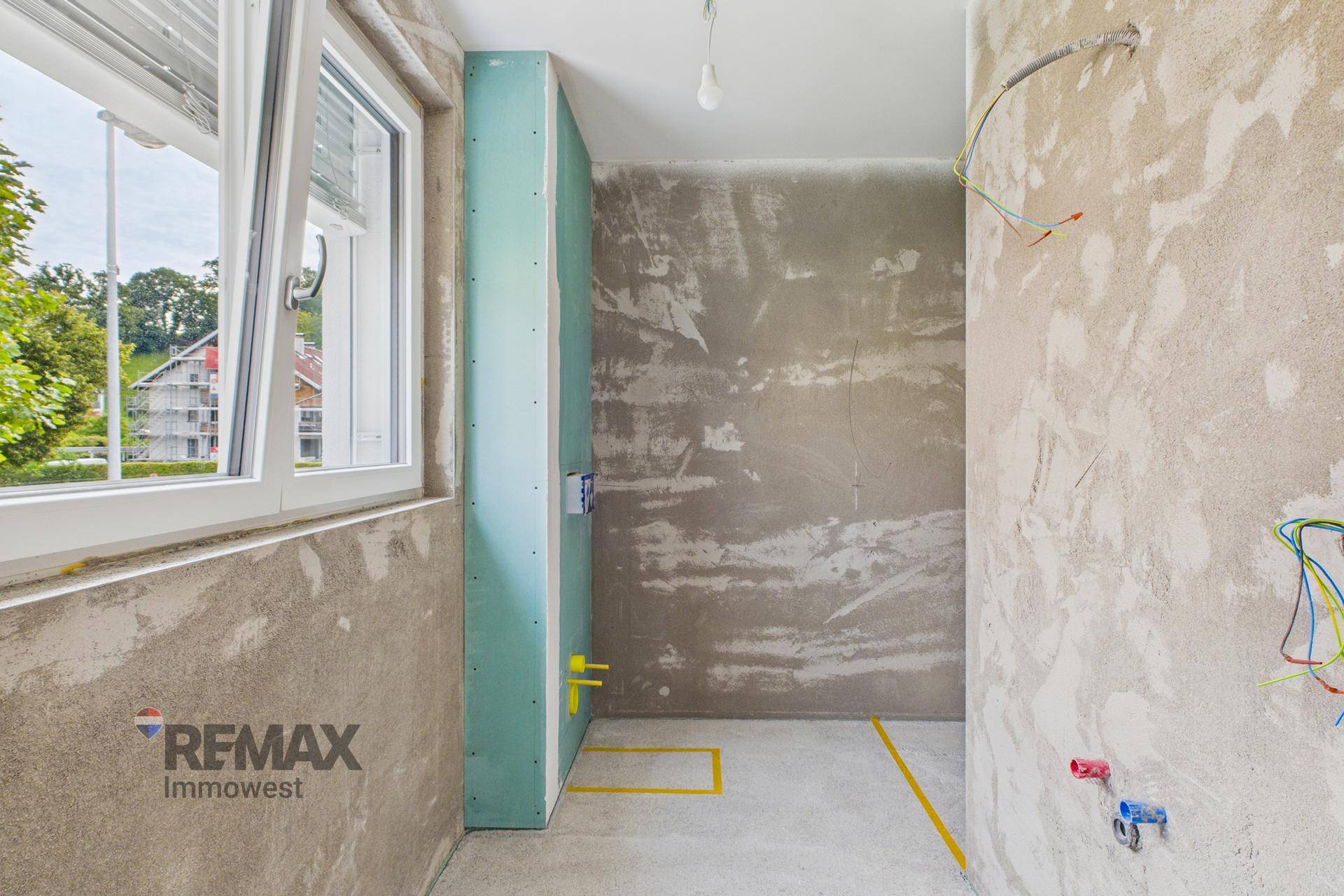 Badezimmer im Rohbauzustand mit Fenster, vorbereitet für Sanitärinstallationen und Fliesenarbeiten.