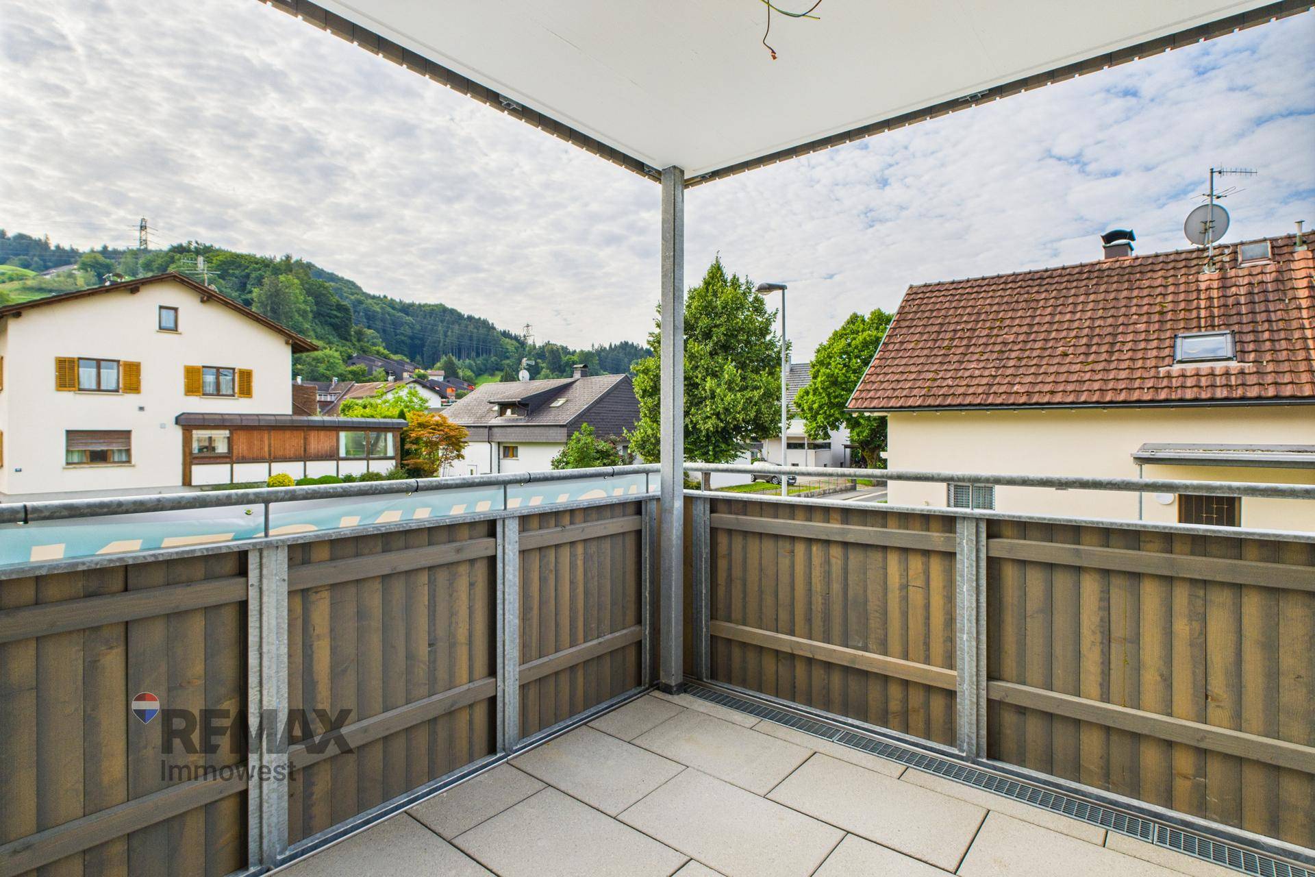 Geräumiger Balkon mit Fliesenboden und Holzelementen, bietet einen grünen Blick auf die Umgebung.
