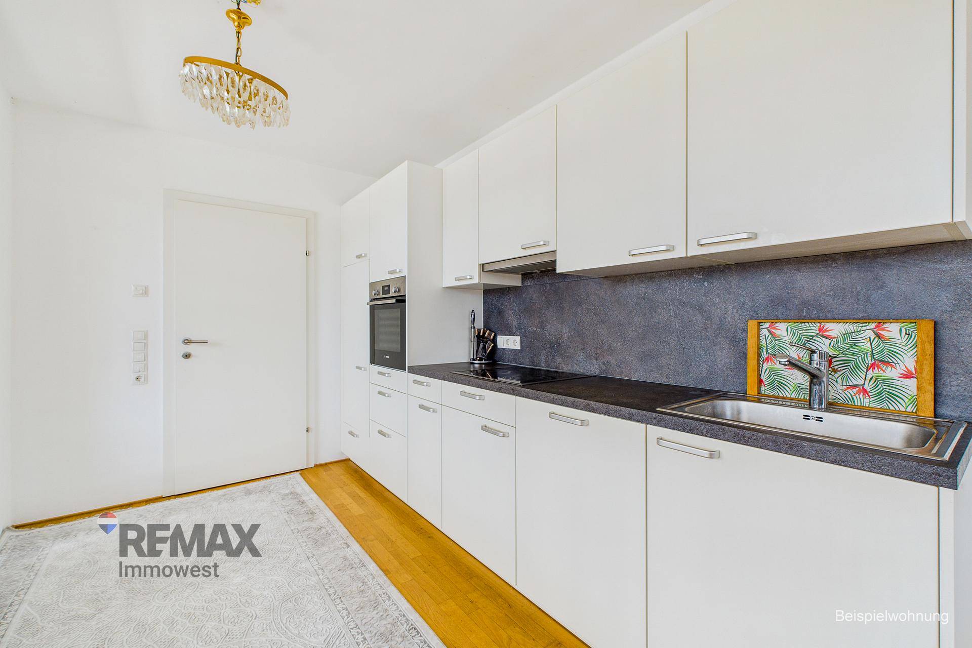 Moderne Einbauküche mit weißen Schränken, dunkler Arbeitsplatte und Holzboden.