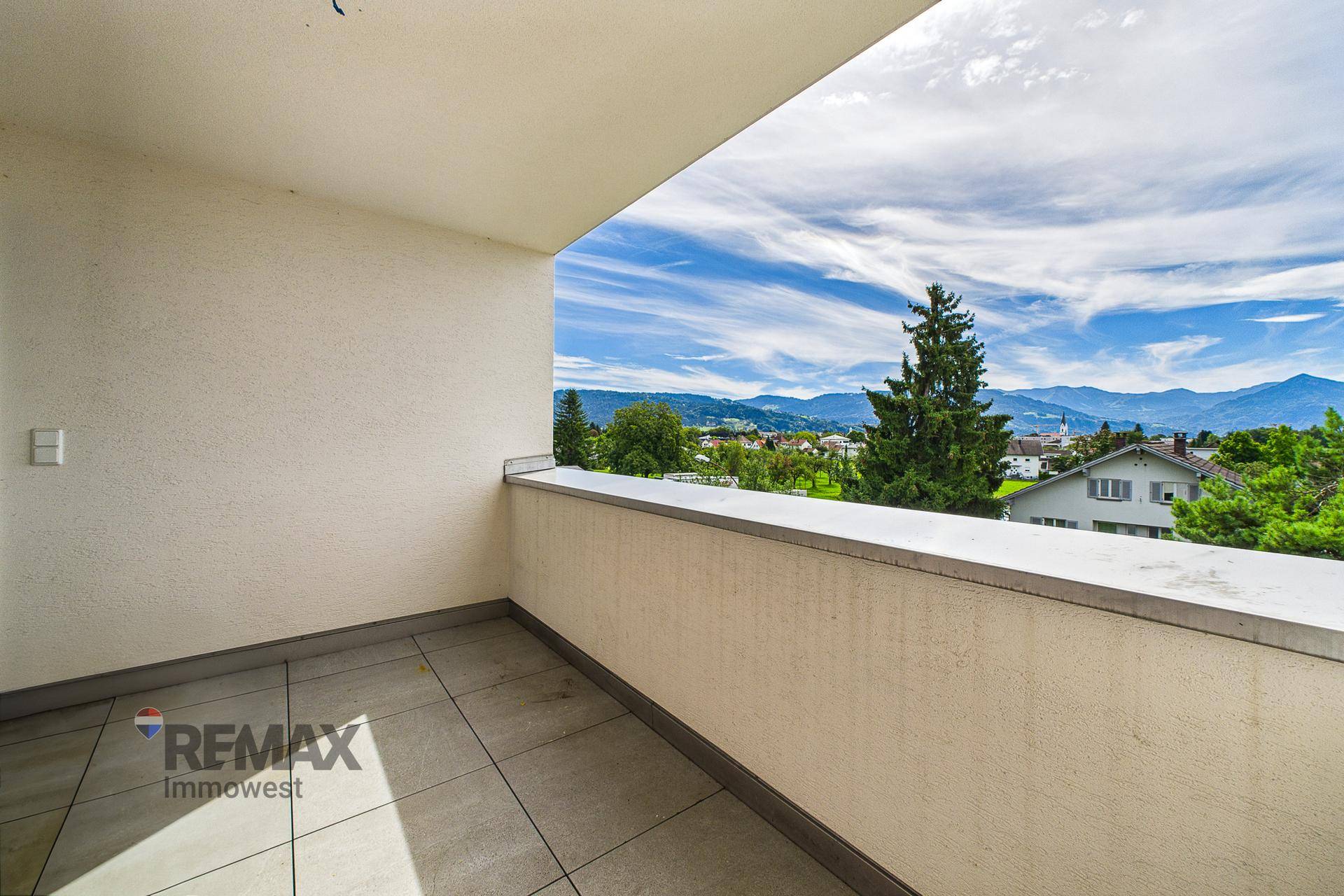 Heller Balkon mit Fliesenboden und weitem Blick auf die grüne Landschaft und Berge.