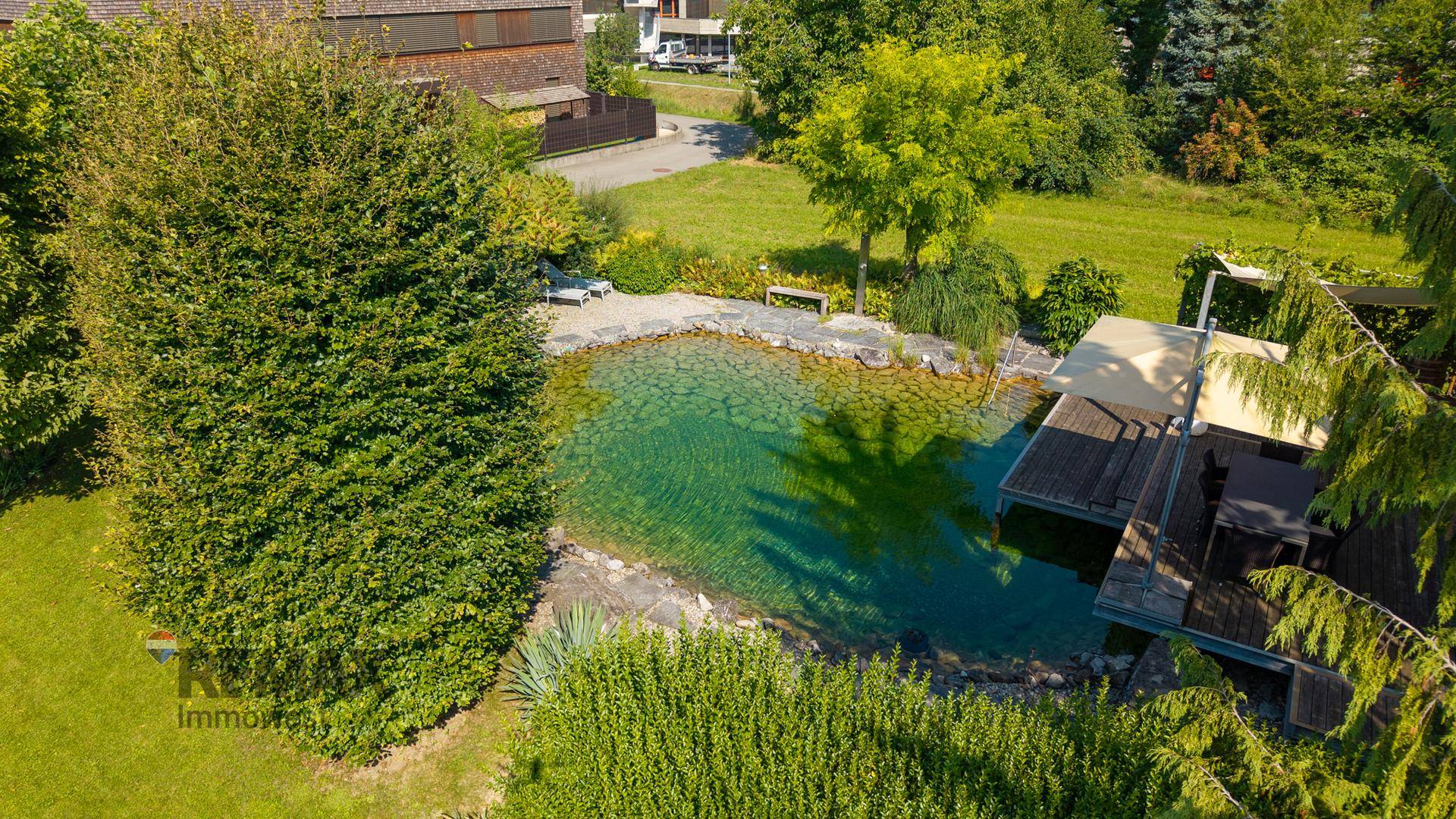 Luftaufnahme des weitläufigen Gartens mit großem Naturteich und angrenzender Holzterrasse.