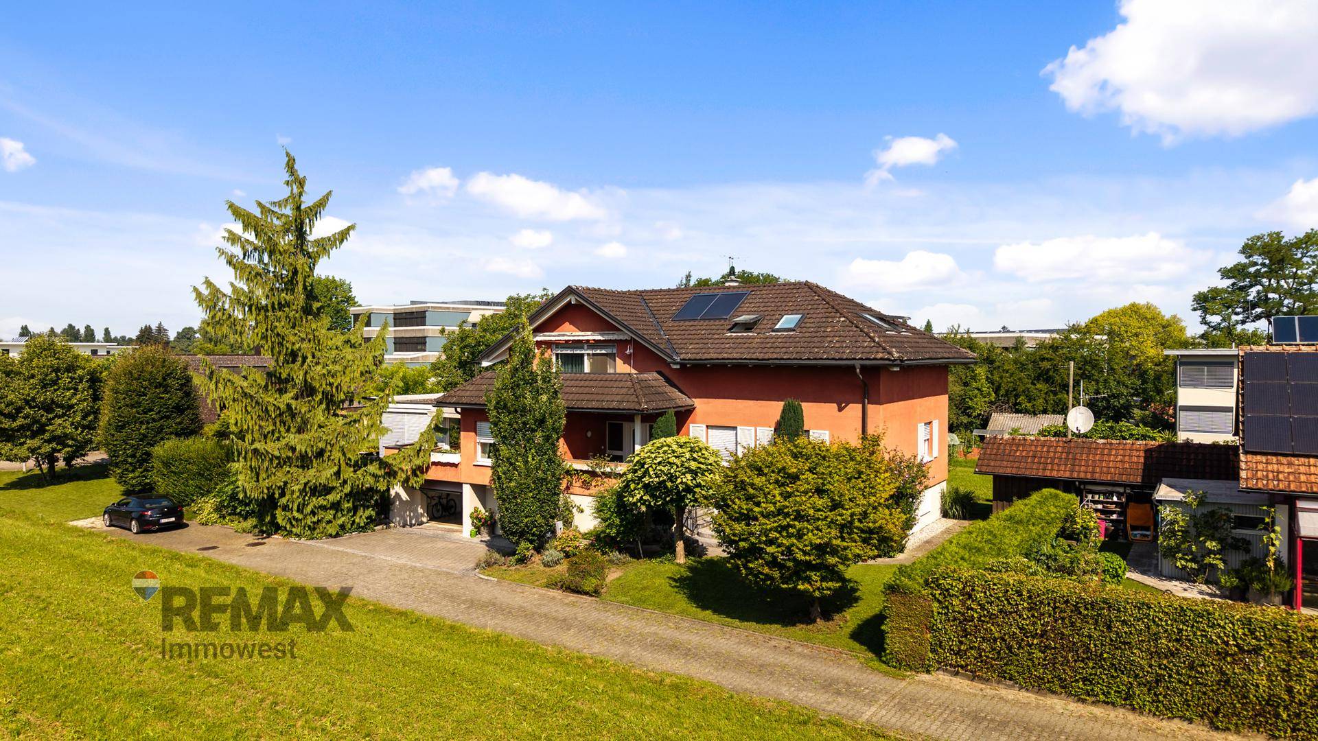 Einfamilienhaus mit rotem Ziegeldach, oranger Fassade und Photovoltaikanlage auf dem Dach.