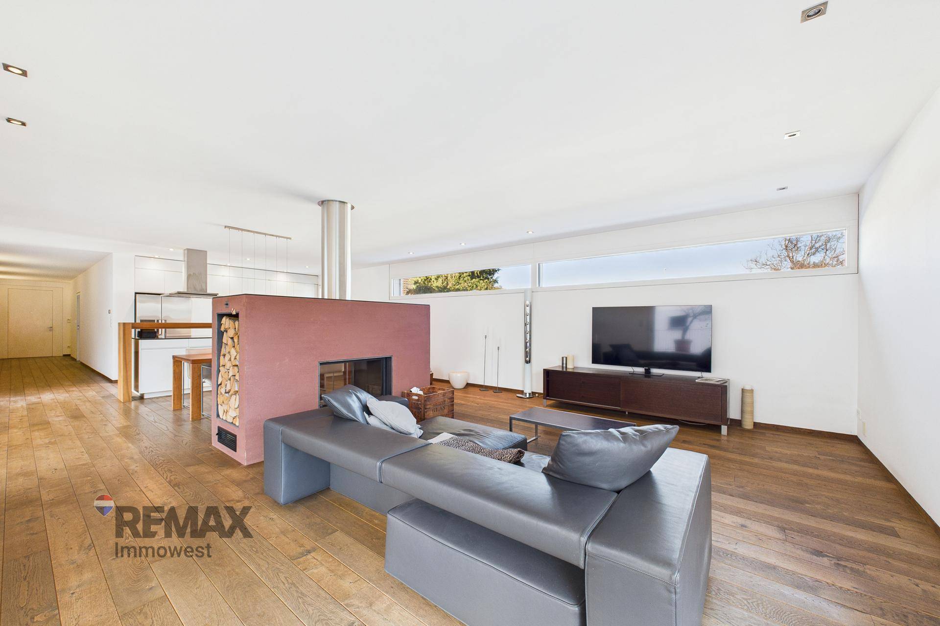 Moderner Wohnbereich mit großem Sofa, Kamin und Blick auf die offene Küche.