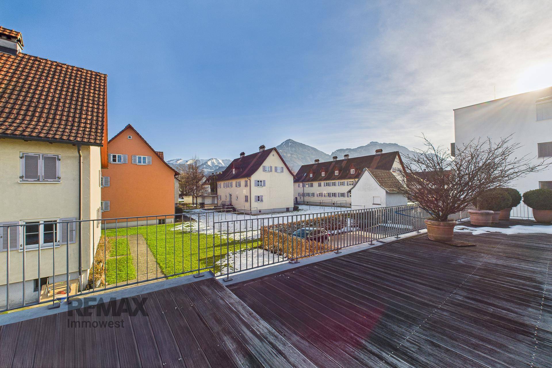 Sonniger Terrassenbereich mit Holzboden und weitem Blick auf die Berge und Nachbarschaft.