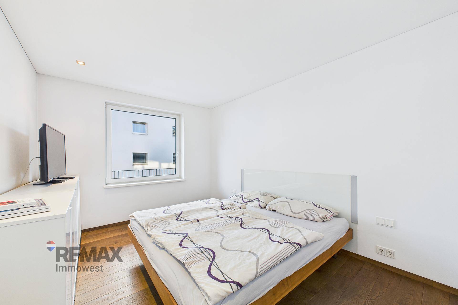 Helles Schlafzimmer mit Holzboden, Doppelbett und einem Fenster mit Blick nach draußen.