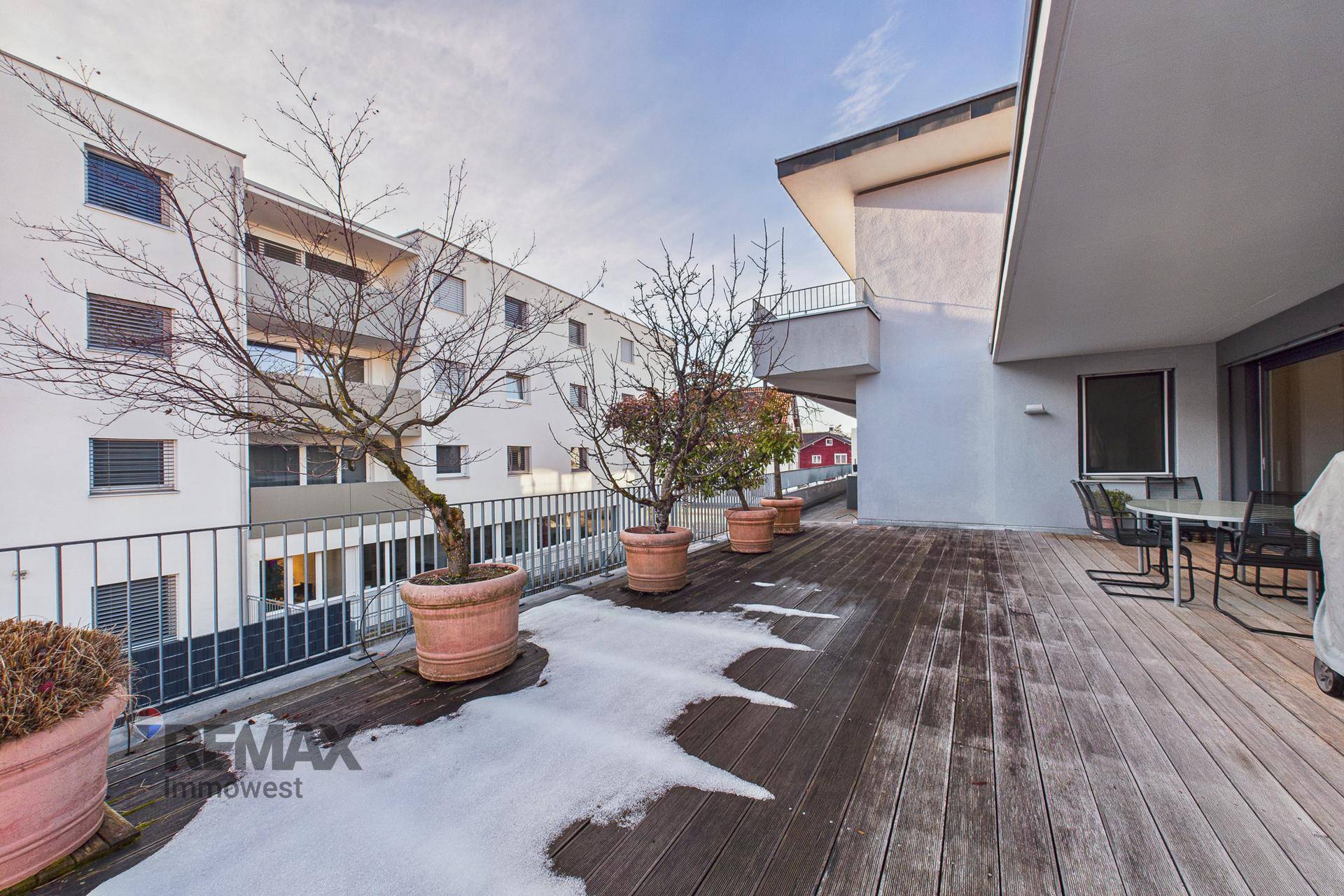 Weitläufige Holzterrasse mit Topfpflanzen und Blick auf die umliegenden Gebäude.