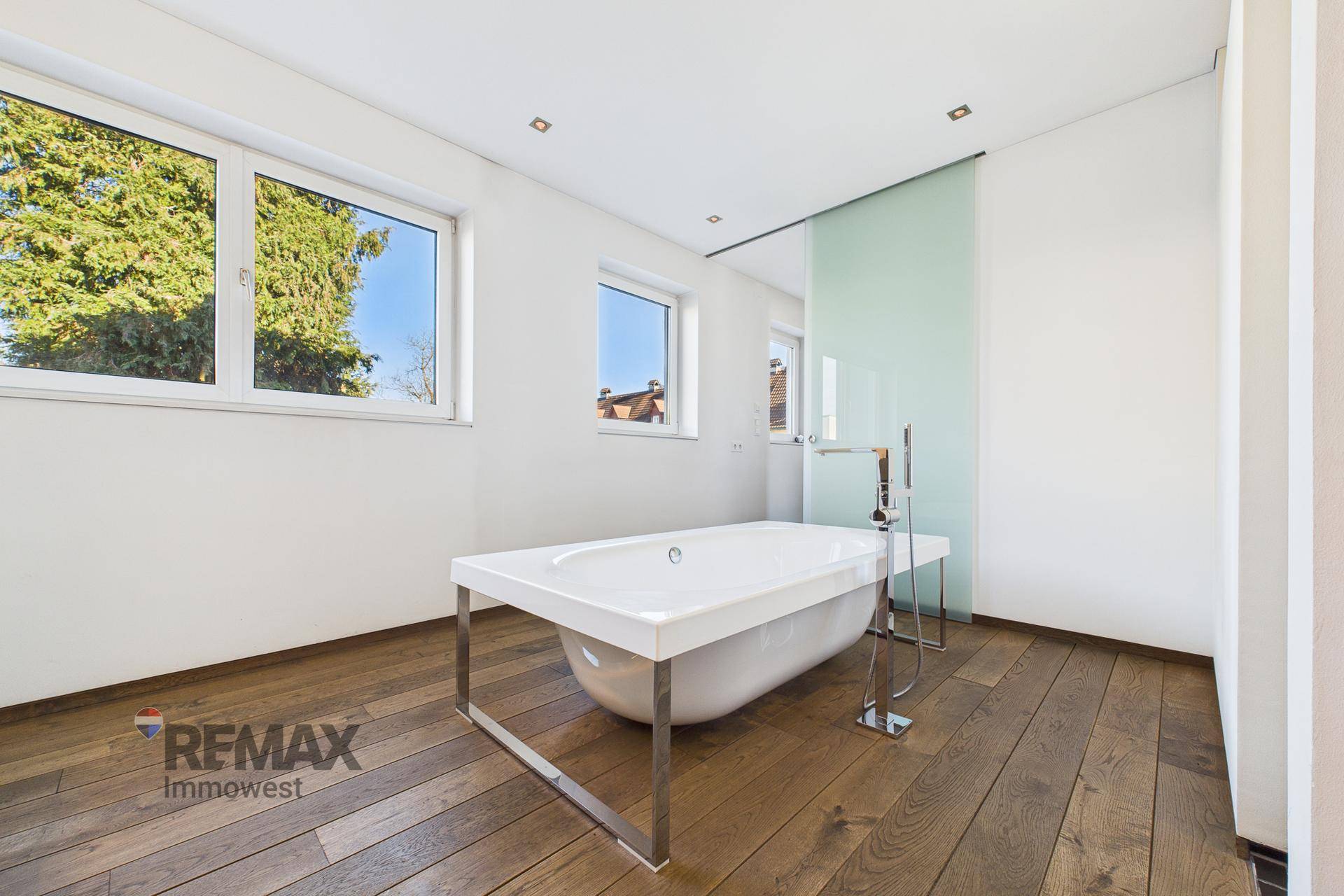 Geräumiges Badezimmer mit freistehender Badewanne und großen Fenstern.