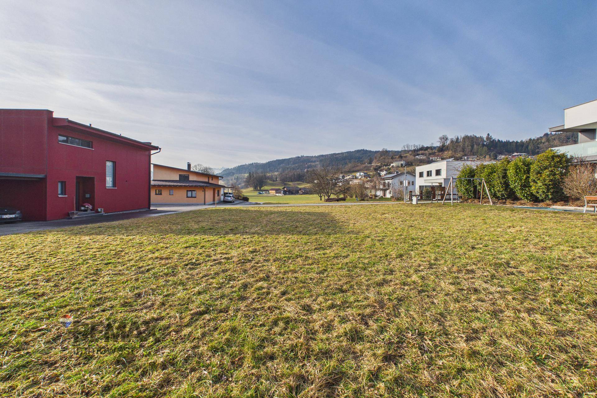 Weitläufige grüne Wiese mit einem markanten roten Haus und weiteren Gebäuden im Hintergrund.