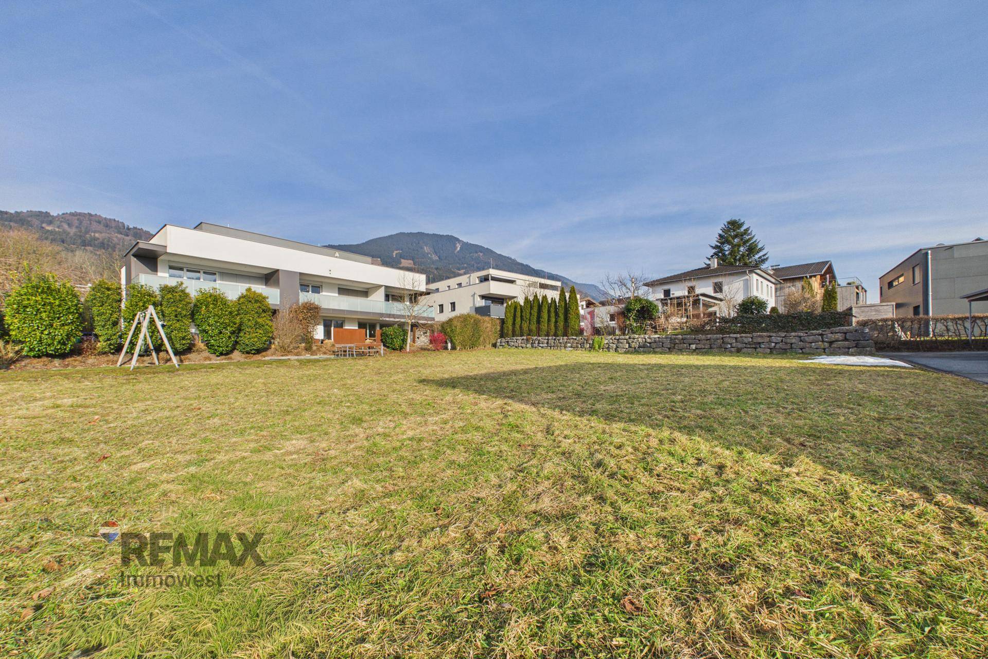 Weitläufige Grünfläche mit modernen Wohngebäuden und einer Bergkette im Hintergrund.