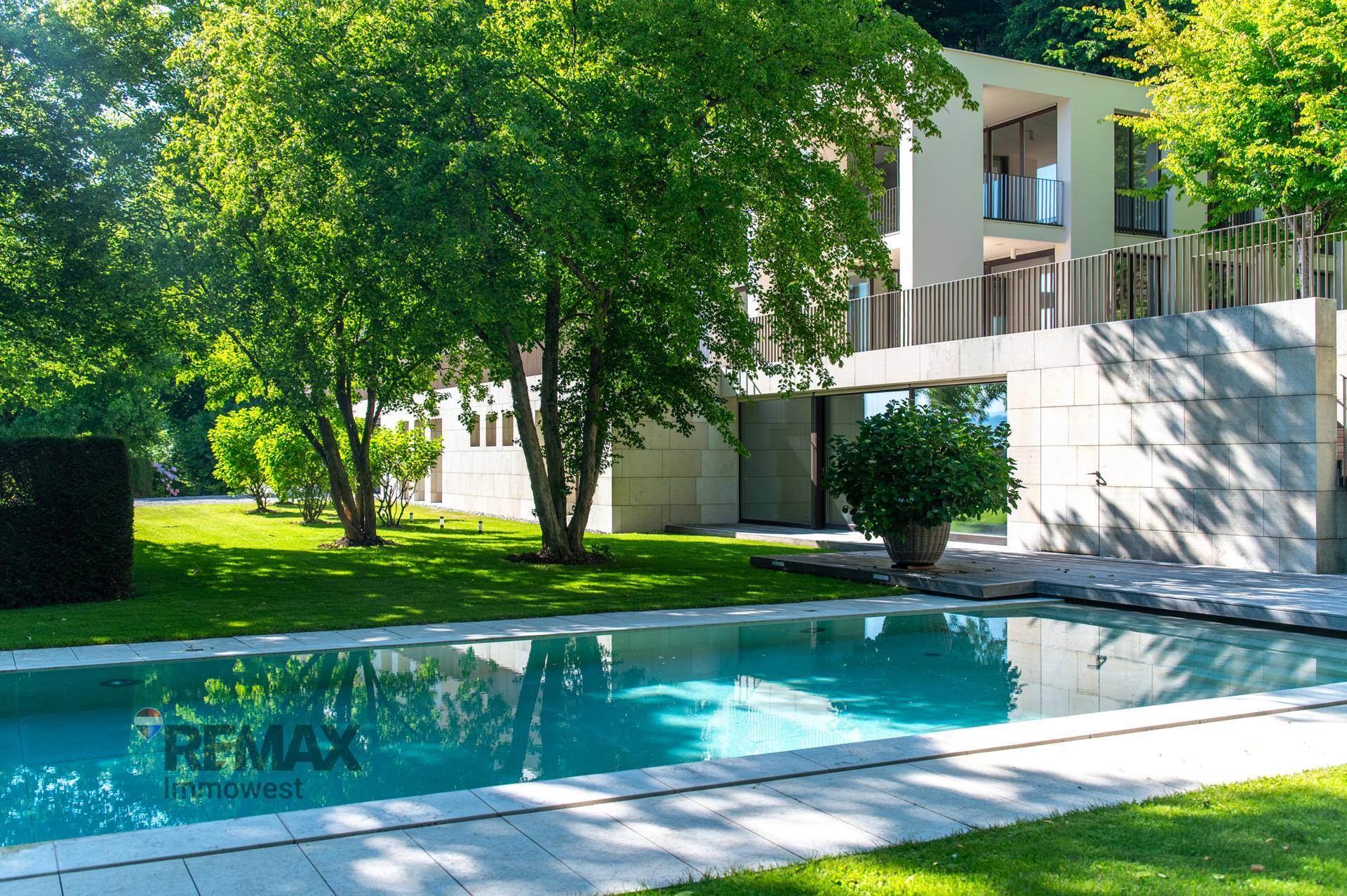 Gepflegter Gartenbereich mit großem Swimmingpool und Liegewiese, umgeben von üppigem Grün und Bäumen.