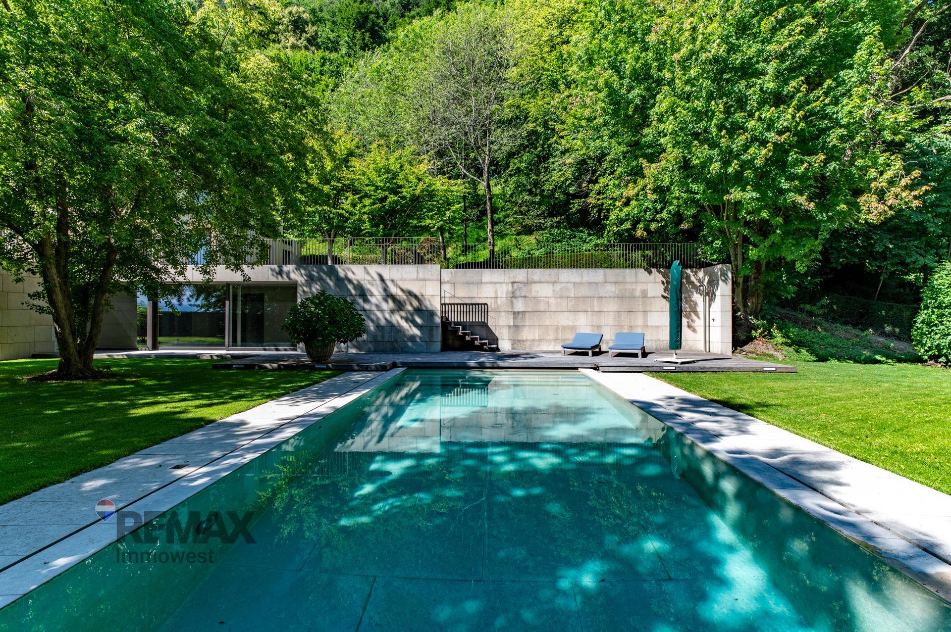 Langer, eleganter Swimmingpool im Garten, umgeben von Rasenflächen und einer Steinmauer im Hintergrund.