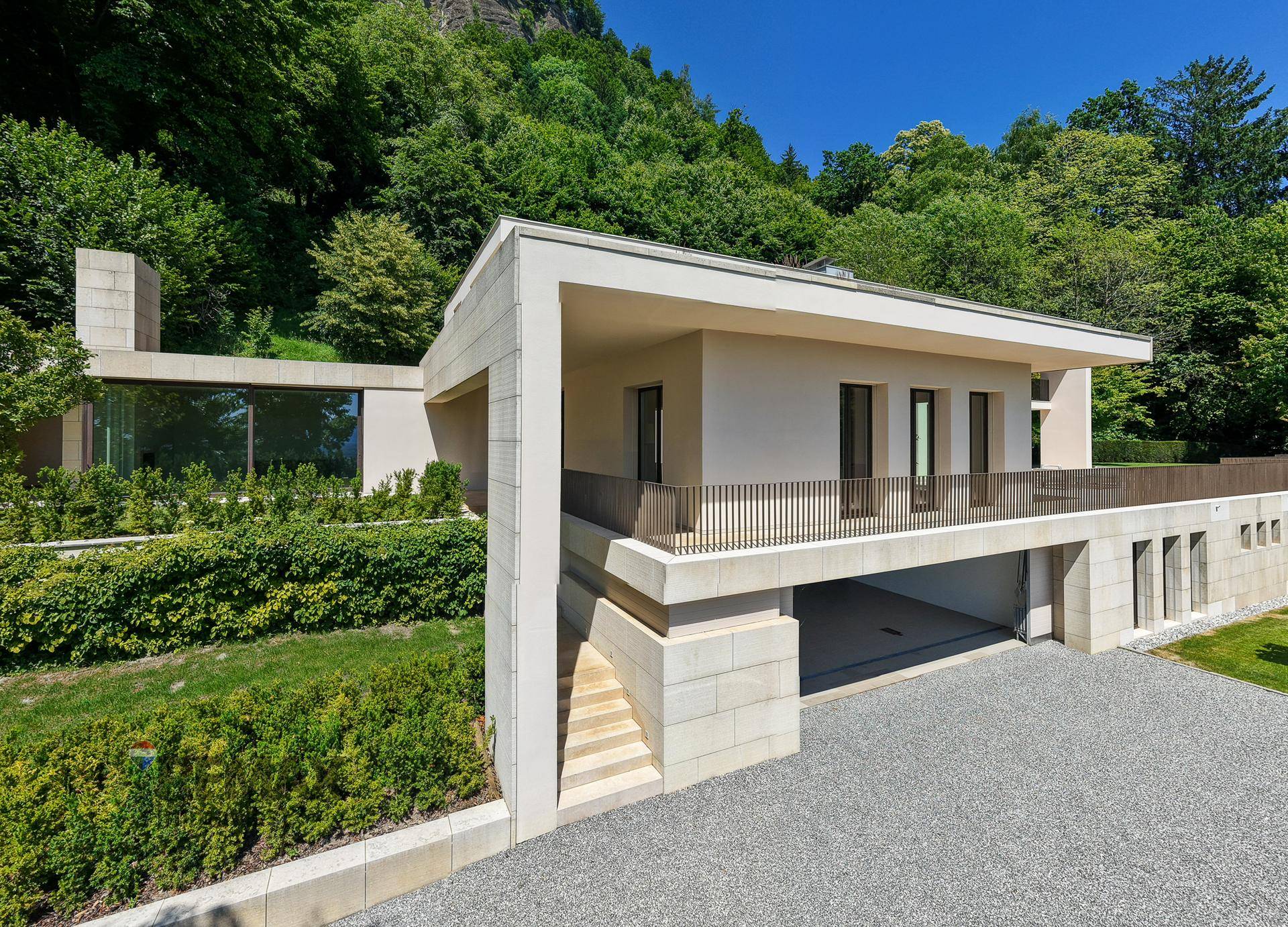 Moderne Architektur der Villa, harmonisch in die grüne Hanglage integriert, mit Zufahrt und Garagenbereich.