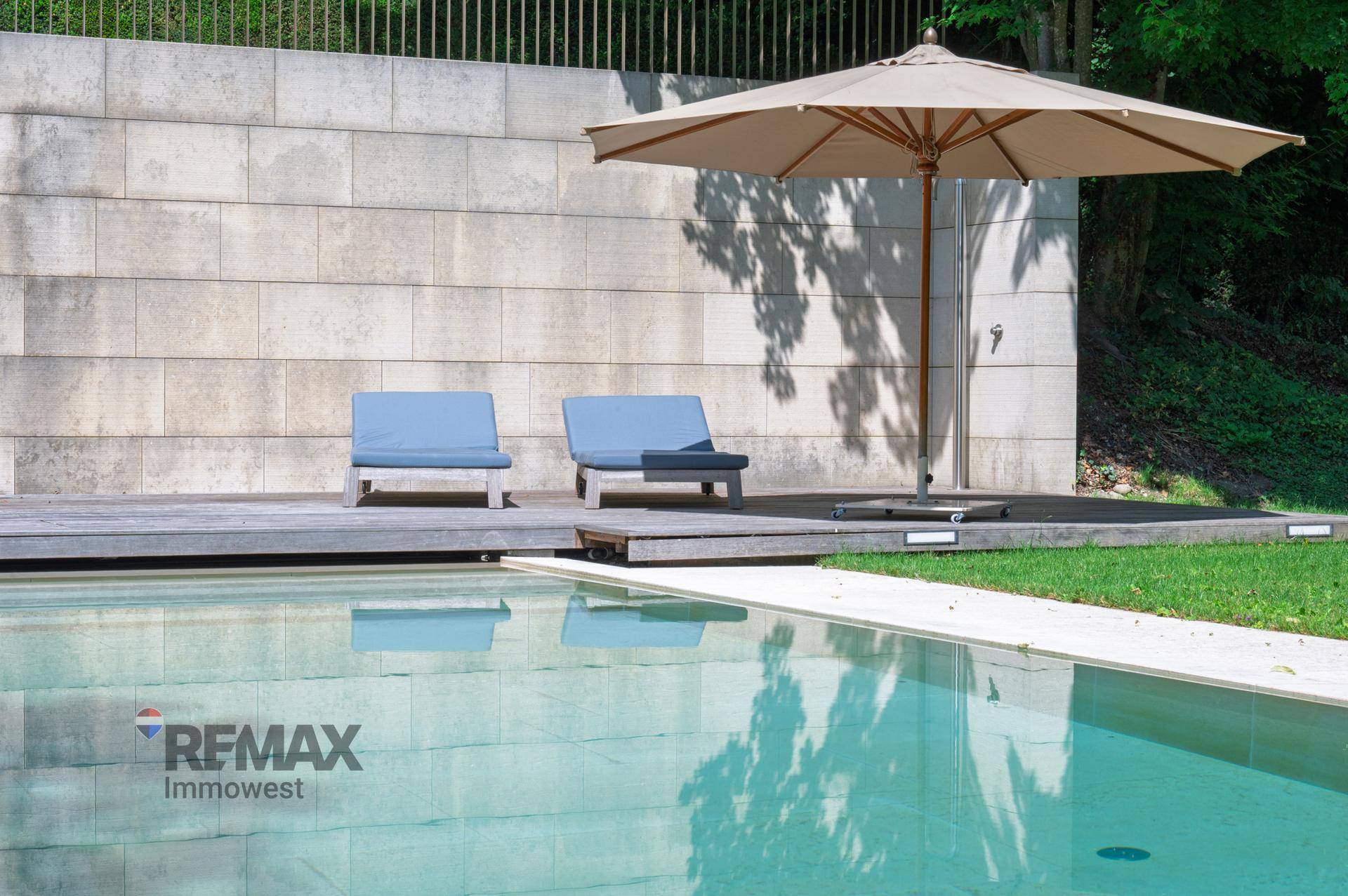 Entspannungsbereich am Pool mit Holzdeck, bequemen Liegestühlen und großem Sonnenschirm.