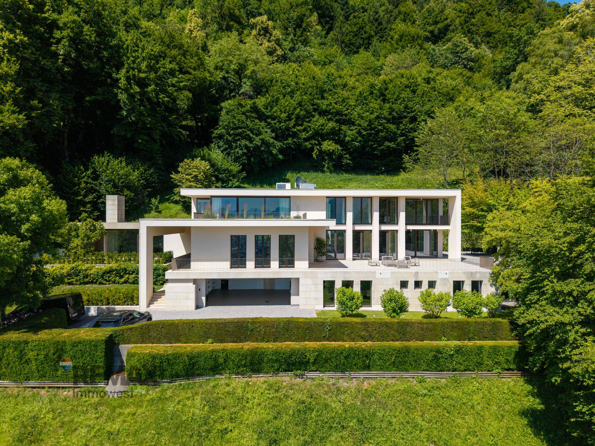 Beeindruckende moderne Villa mit Flachdach und weitläufigen Terrassen, eingebettet in eine grüne Hügellandschaft.