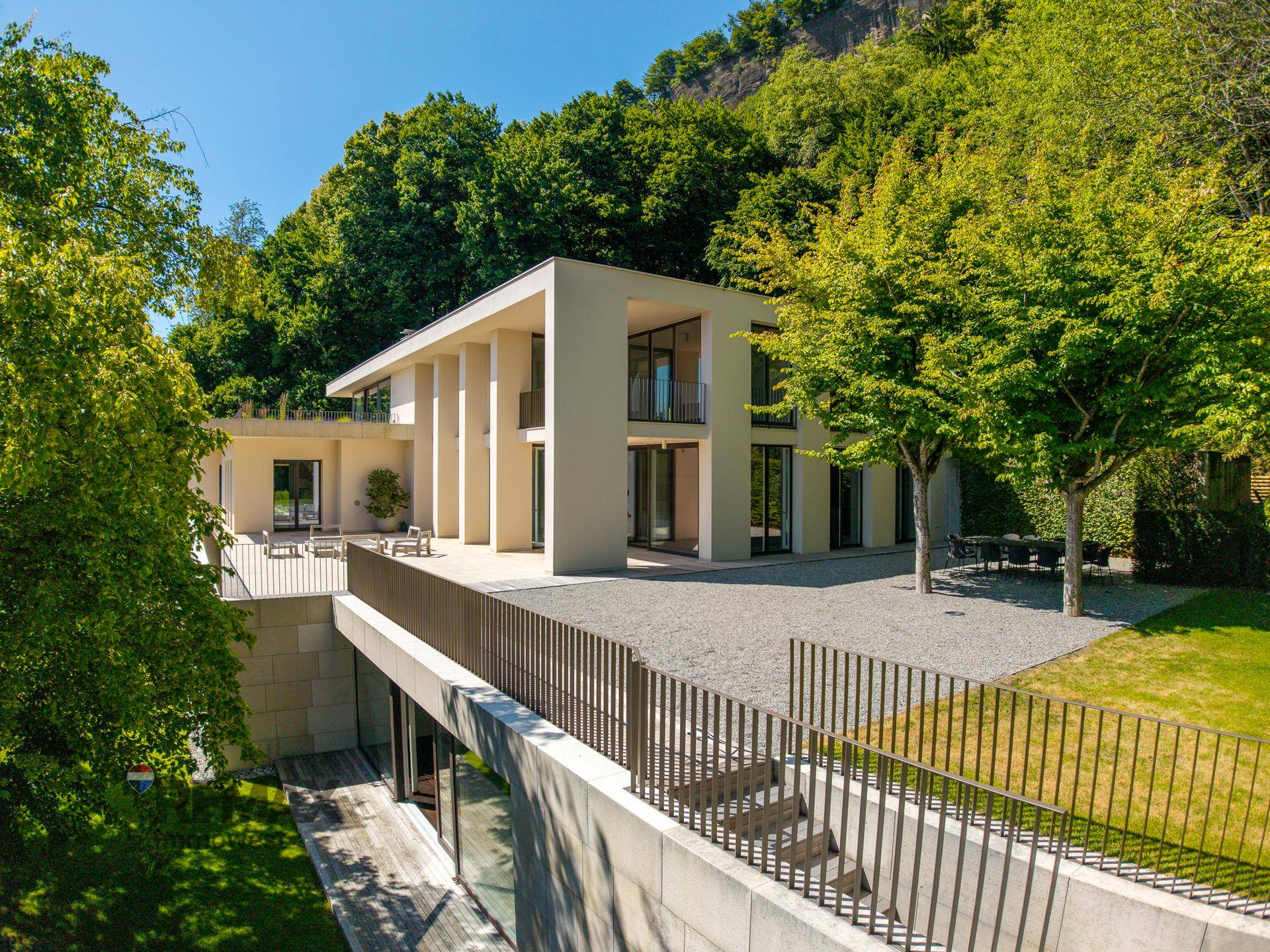 Elegante moderne Villa mit großzügigen Terrassen und gepflegter Außenanlage, umgeben von altem Baumbestand.