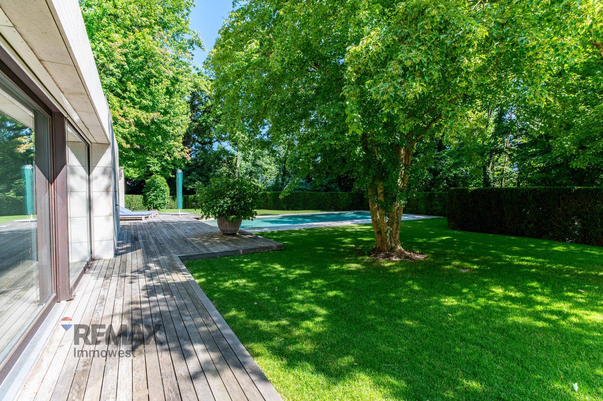 Sonnige Holzterrasse mit Zugang zum weitläufigen Garten und Blick auf den Poolbereich.
