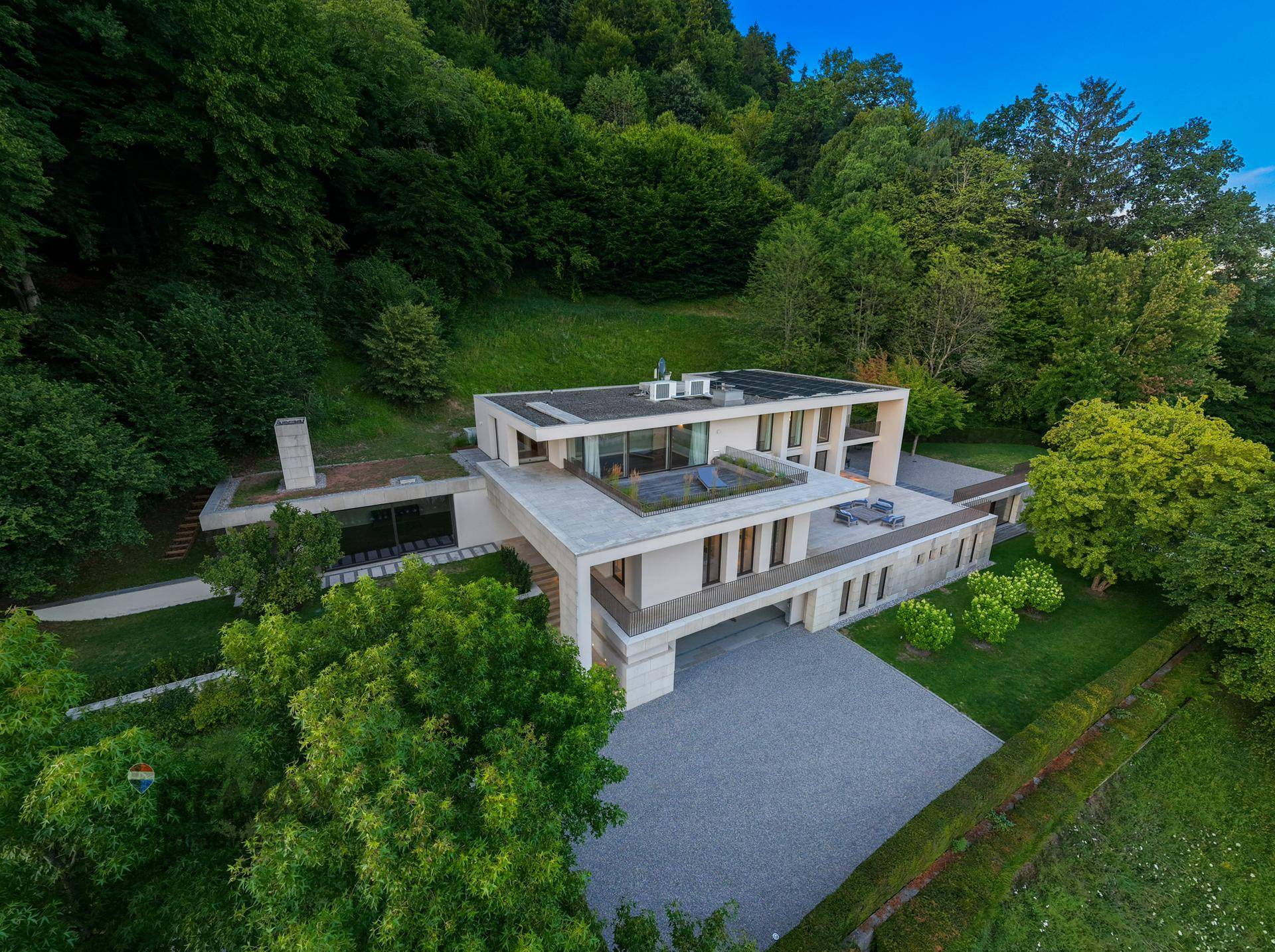 Luftaufnahme der weitläufigen modernen Villa mit Flachdach und Terrassen, eingebettet in die Natur.