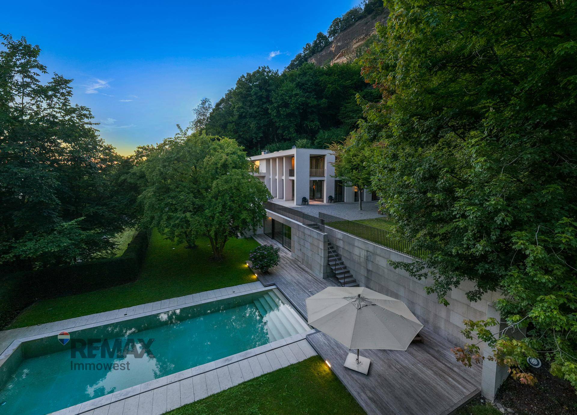 Abendliche Ansicht der Villa mit beleuchtetem Poolbereich und gemütlicher Holzterrasse unter freiem Himmel.