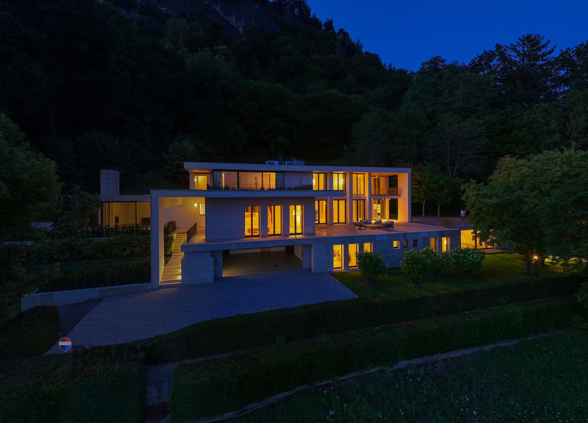 Beeindruckende moderne Villa bei Nacht, mit warm beleuchteten Innenräumen und klaren architektonischen Linien.
