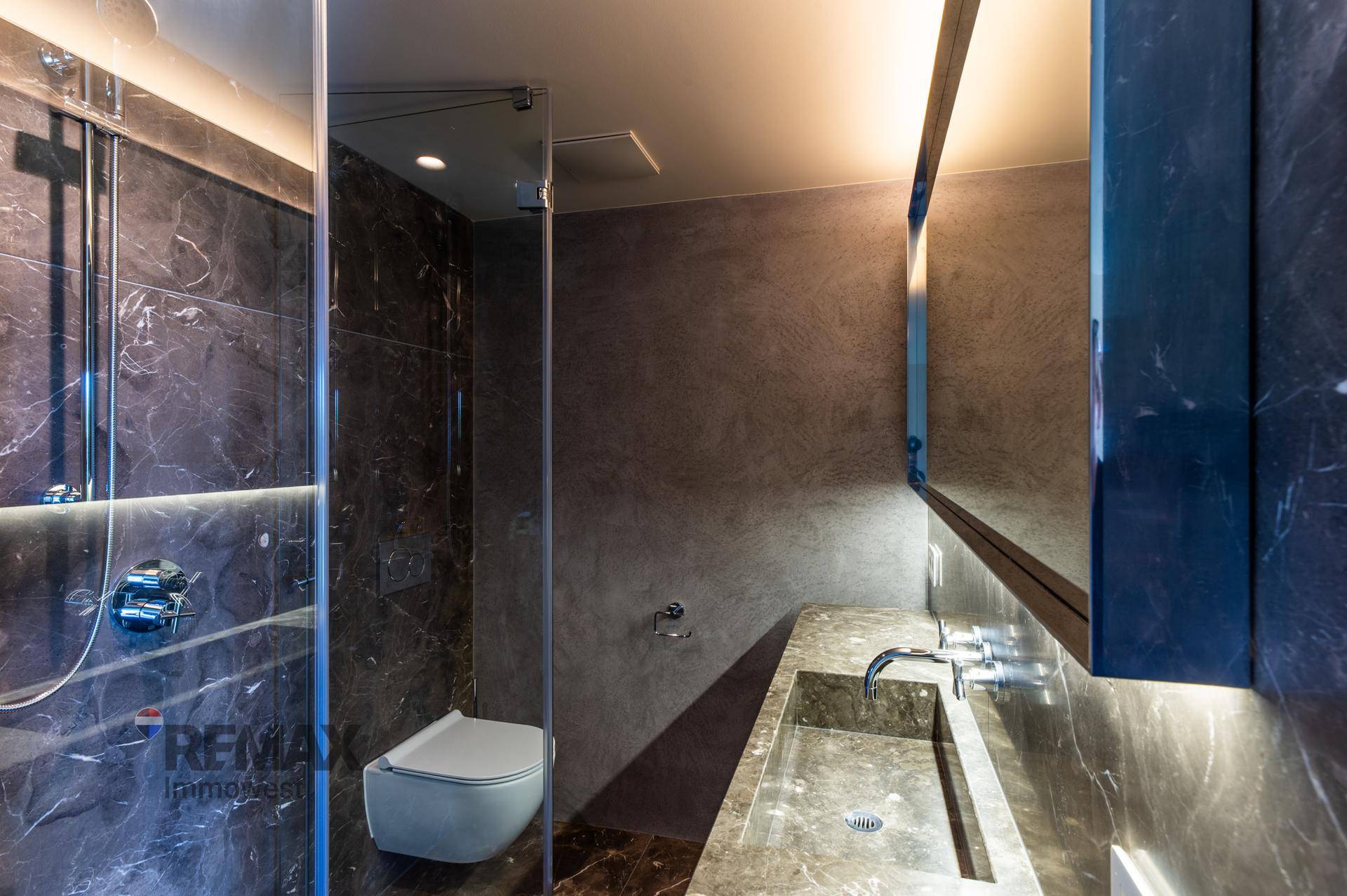 Modernes Badezimmer mit dunklen Marmorfliesen, Dusche und wandhängendem WC.