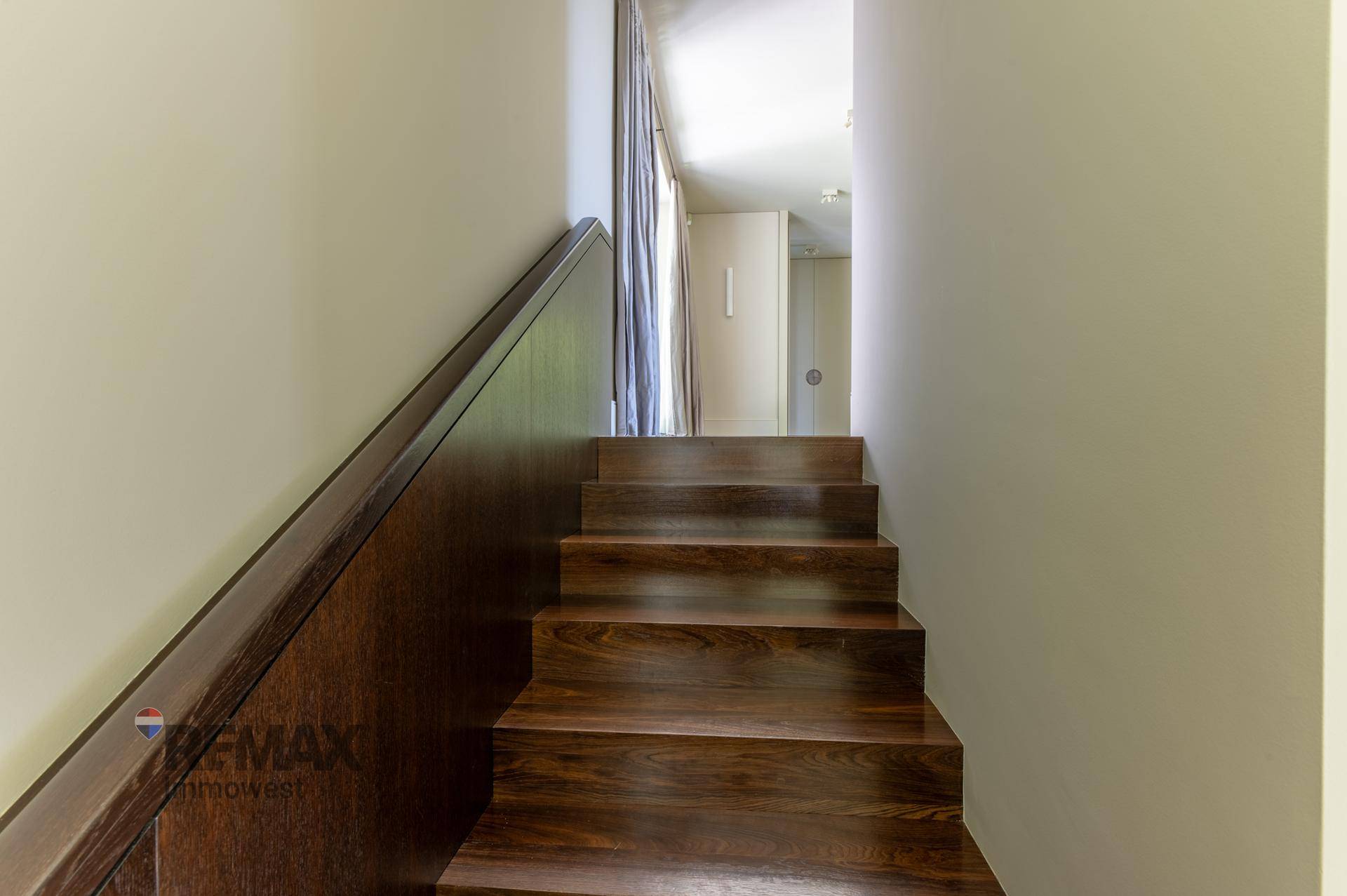 Holztreppe führt zu den oberen Etagen, mit dunklem Holz und hellem Wanddesign.