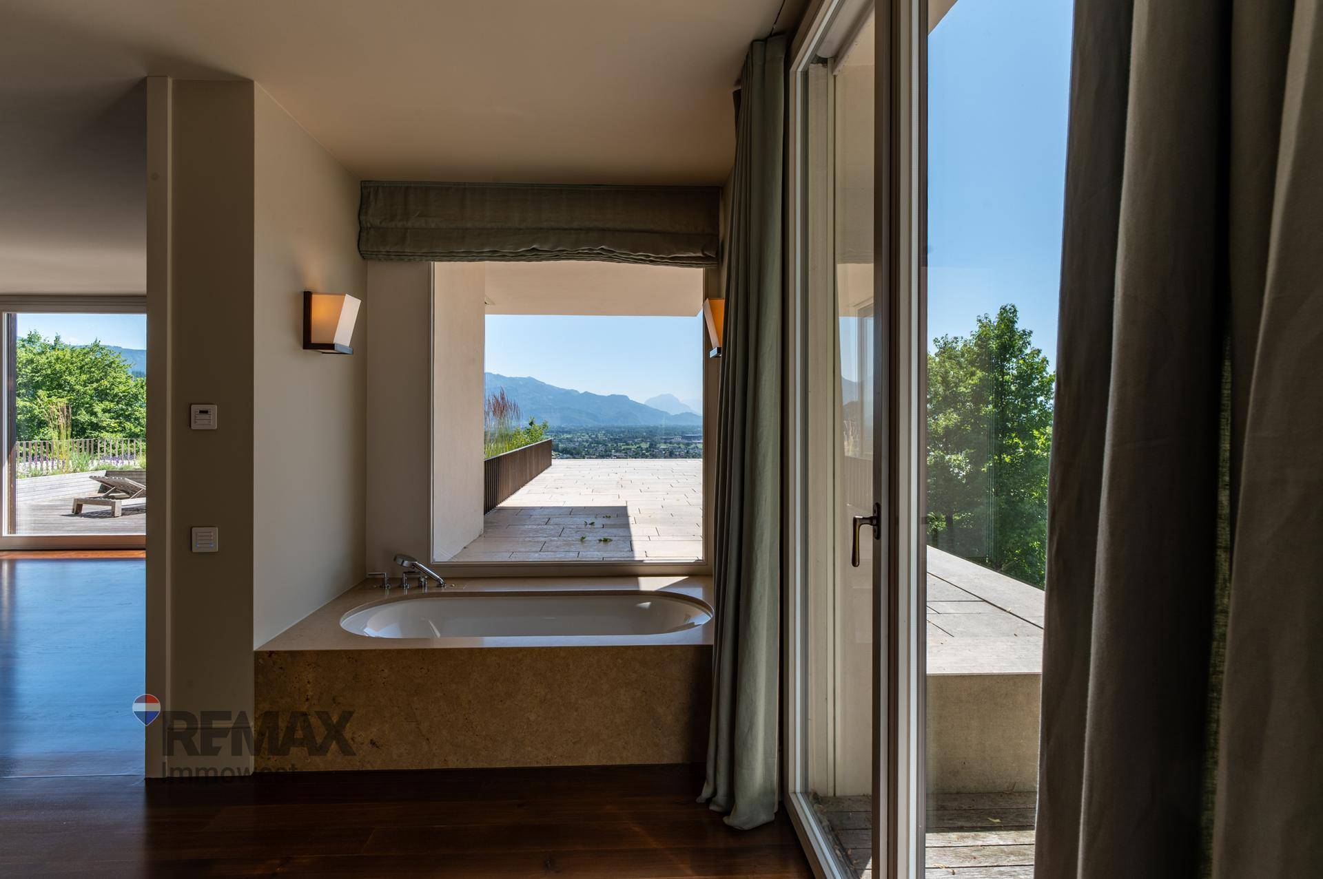 Badezimmer mit Badewanne, Holzboden und großem Fenster mit Bergblick.