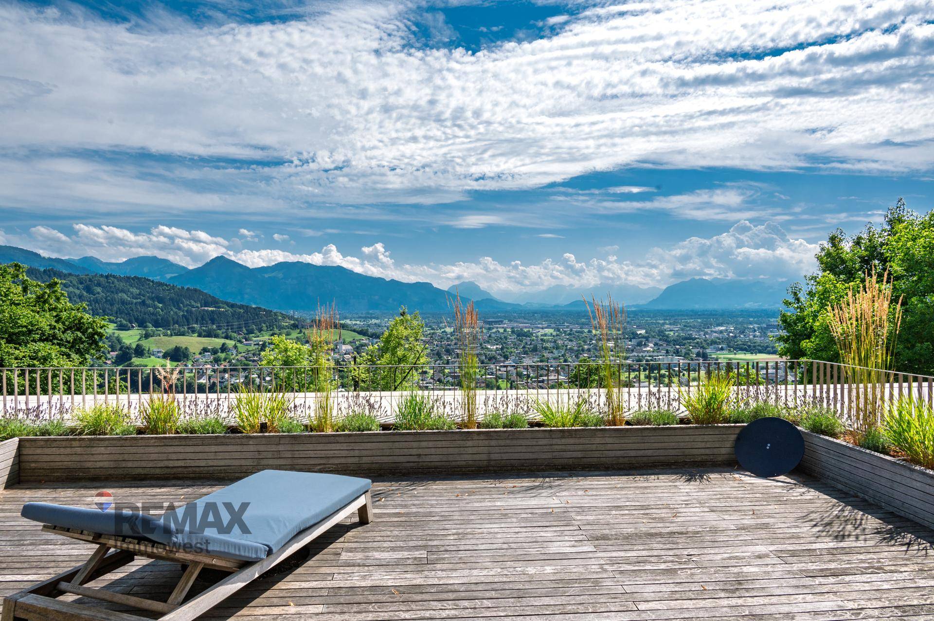 Weitläufige Holzterrasse mit Sonnenliege und beeindruckendem Blick auf die Berge.