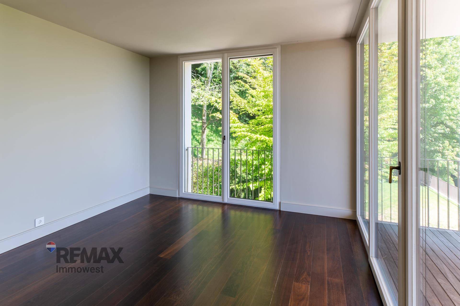 Schlafzimmer mit dunklem Holzboden und Zugang zu einem französischen Balkon.