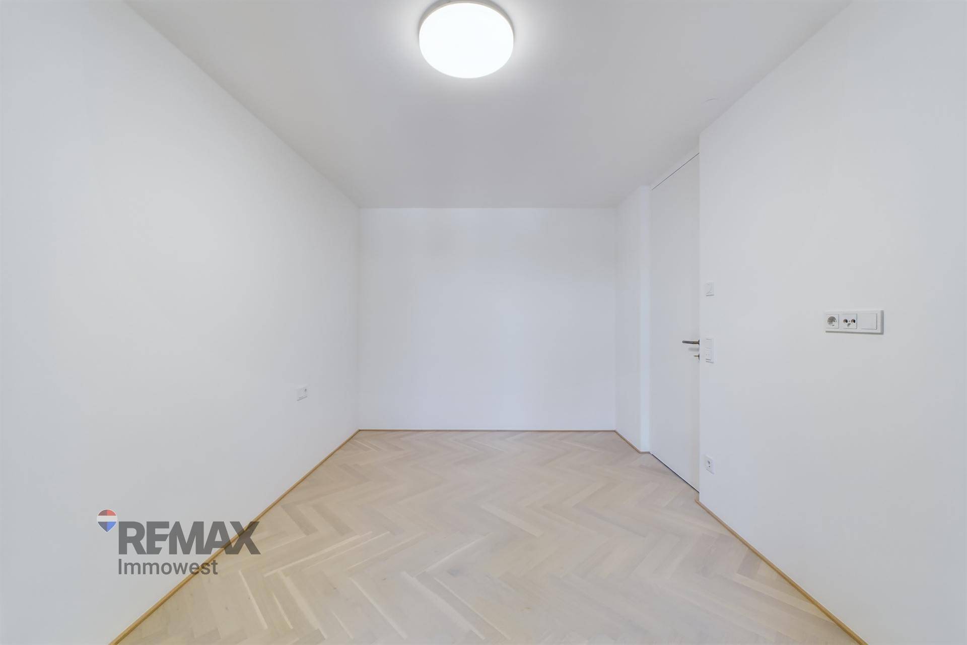 Leeres Zimmer mit weißen Wänden und hellem Fischgrätparkett, bereit zur individuellen Gestaltung.