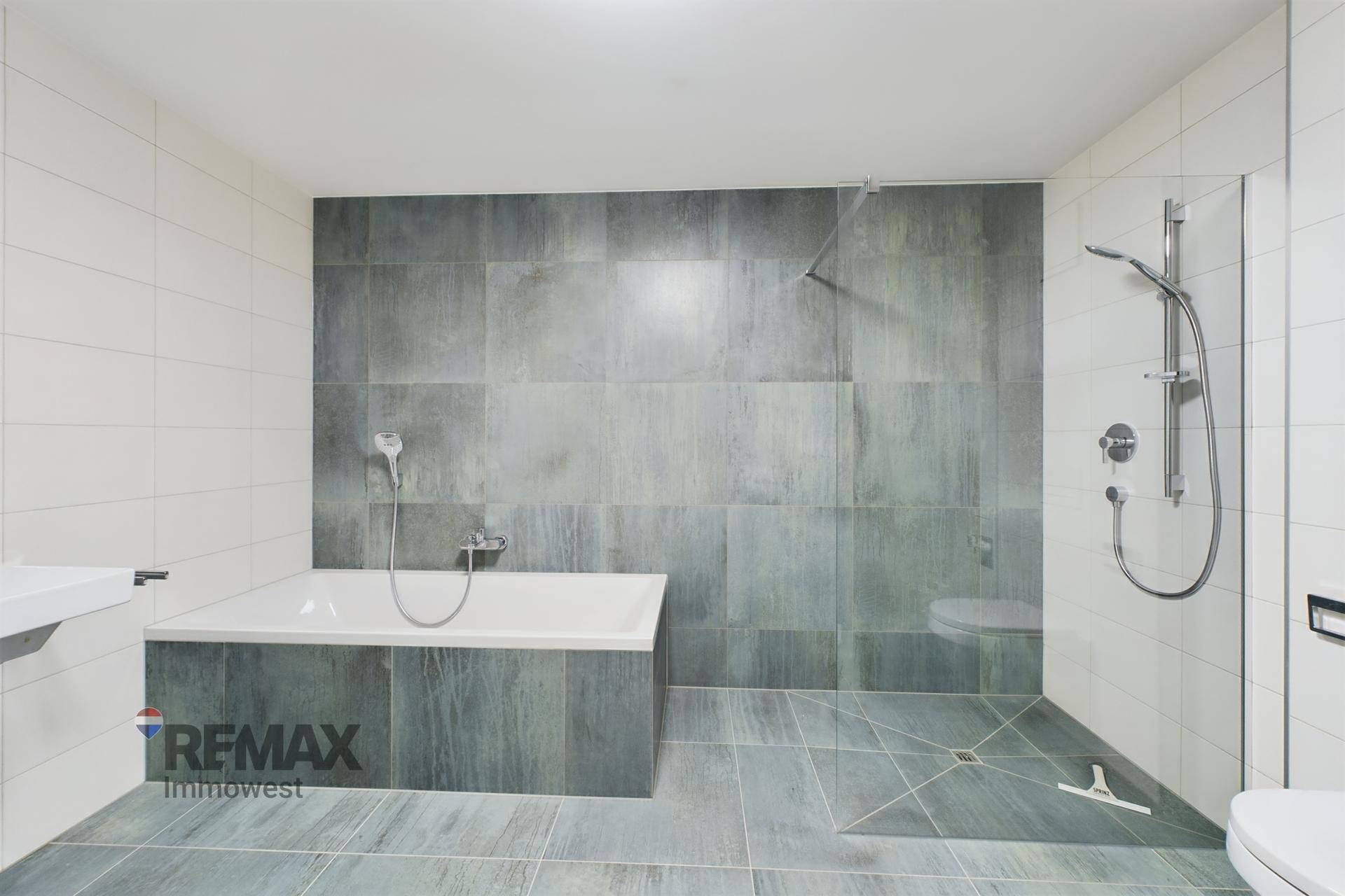 Geräumiges Badezimmer mit modernen grauen Fliesen, begehbarer Dusche und Badewanne.