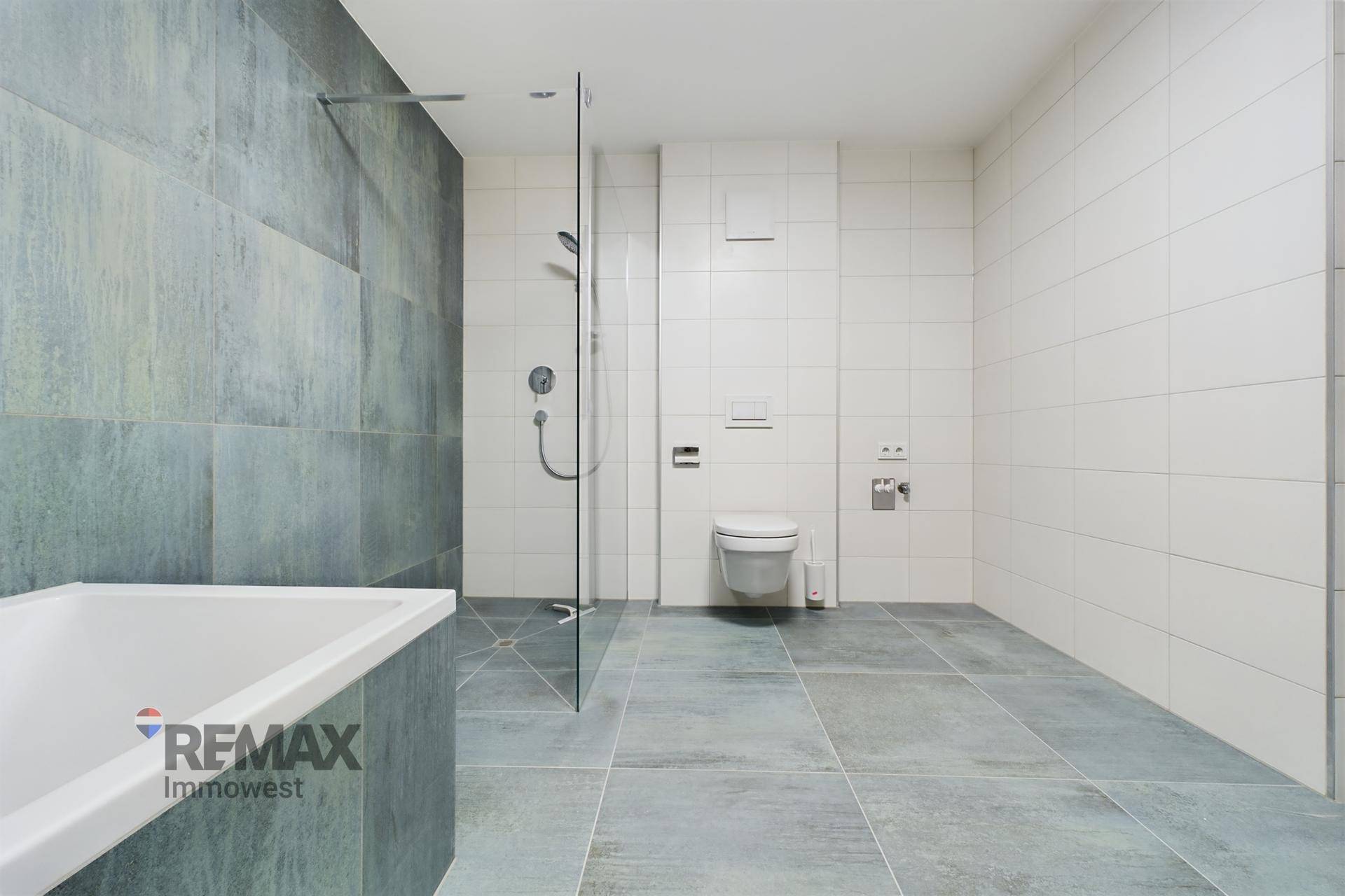 Modernes Badezimmer mit großen grauen Fliesen, begehbarer Dusche und integrierter Badewanne.