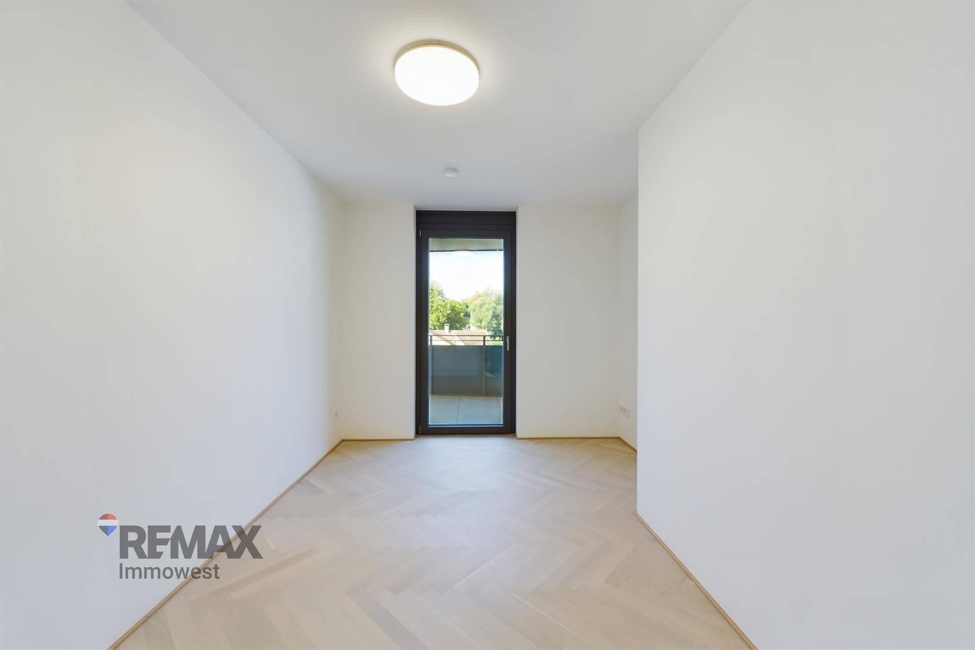 Lichtdurchflutetes Zimmer mit hellem Fischgrätparkett und direktem Zugang zum Balkon.