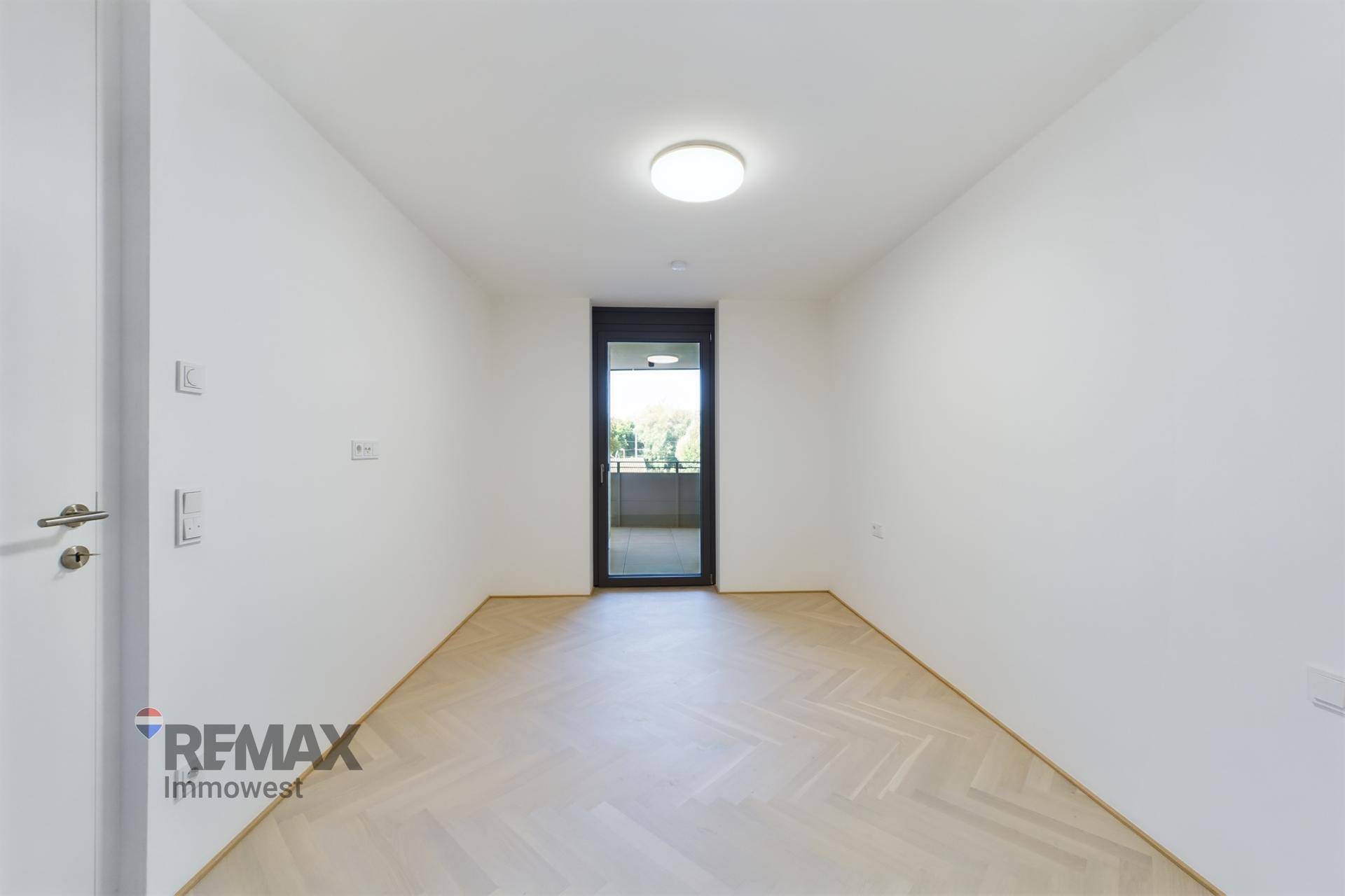 Helles Zimmer mit Fischgrätparkett und großer Glastür, die auf einen Balkon führt.
