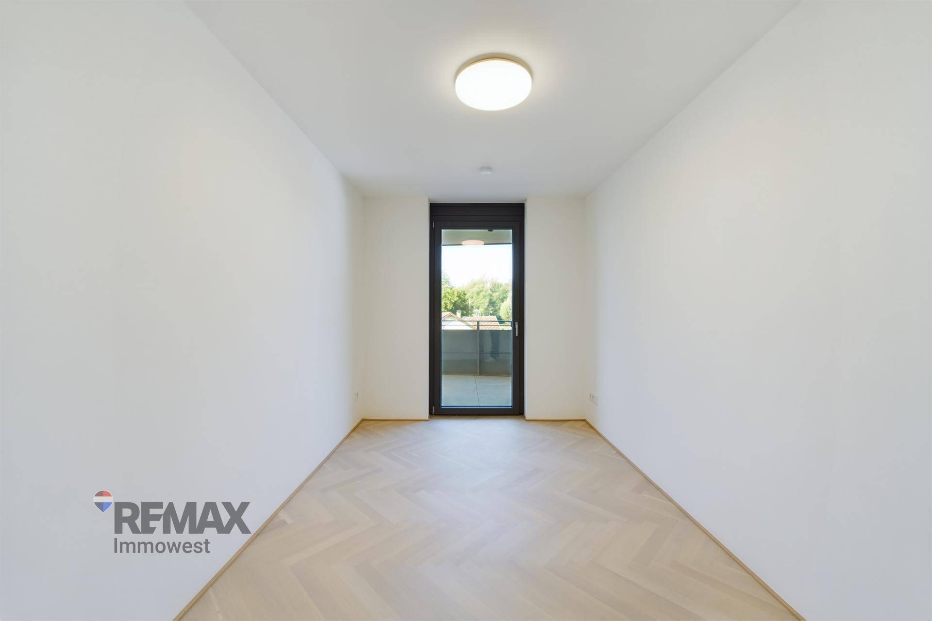 Geräumiges Zimmer mit Fischgrätparkett und bodentiefer Glastür zum Außenbereich.