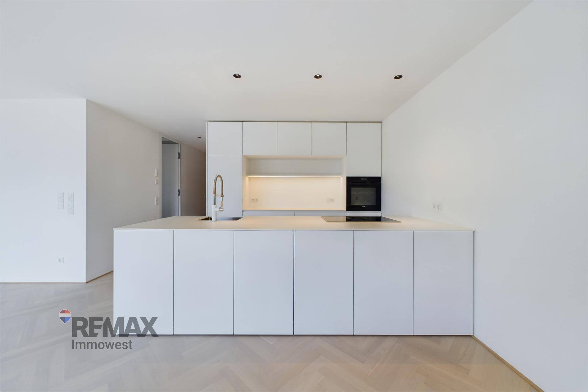 Moderne, minimalistische Küche mit weißen Schränken, Kücheninsel und integriertem Backofen.