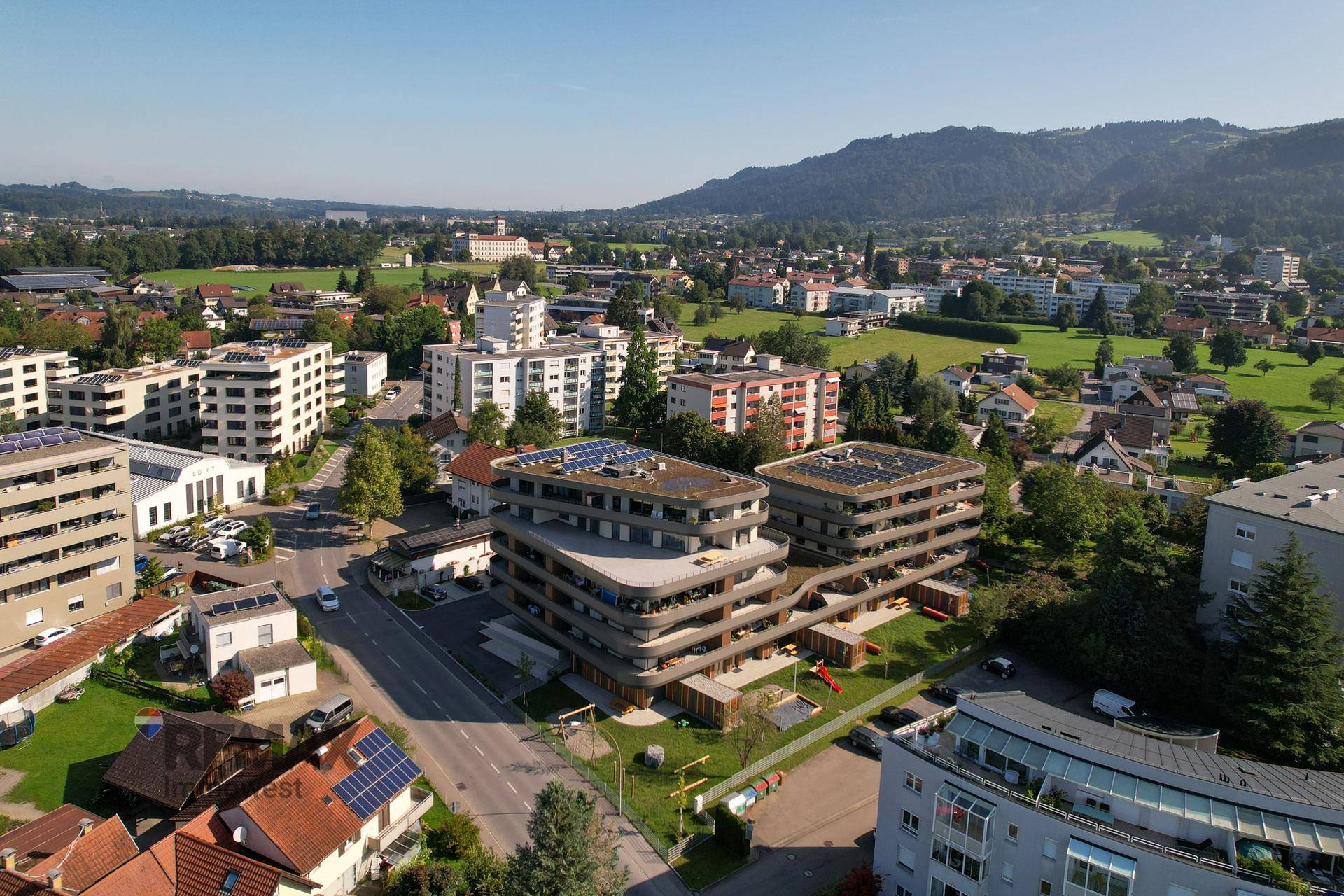 Weitläufige Luftaufnahme einer modernen Wohnanlage mit Gründächern, Solaranlagen und grüner Umgebung.