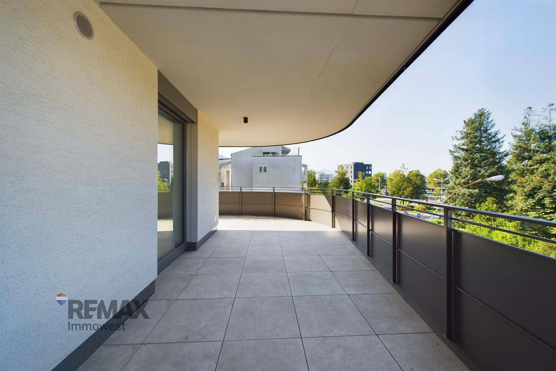 Geräumiger, geschwungener Balkon mit Fliesenboden und Blick ins Grüne, ideal für sonnige Stunden.