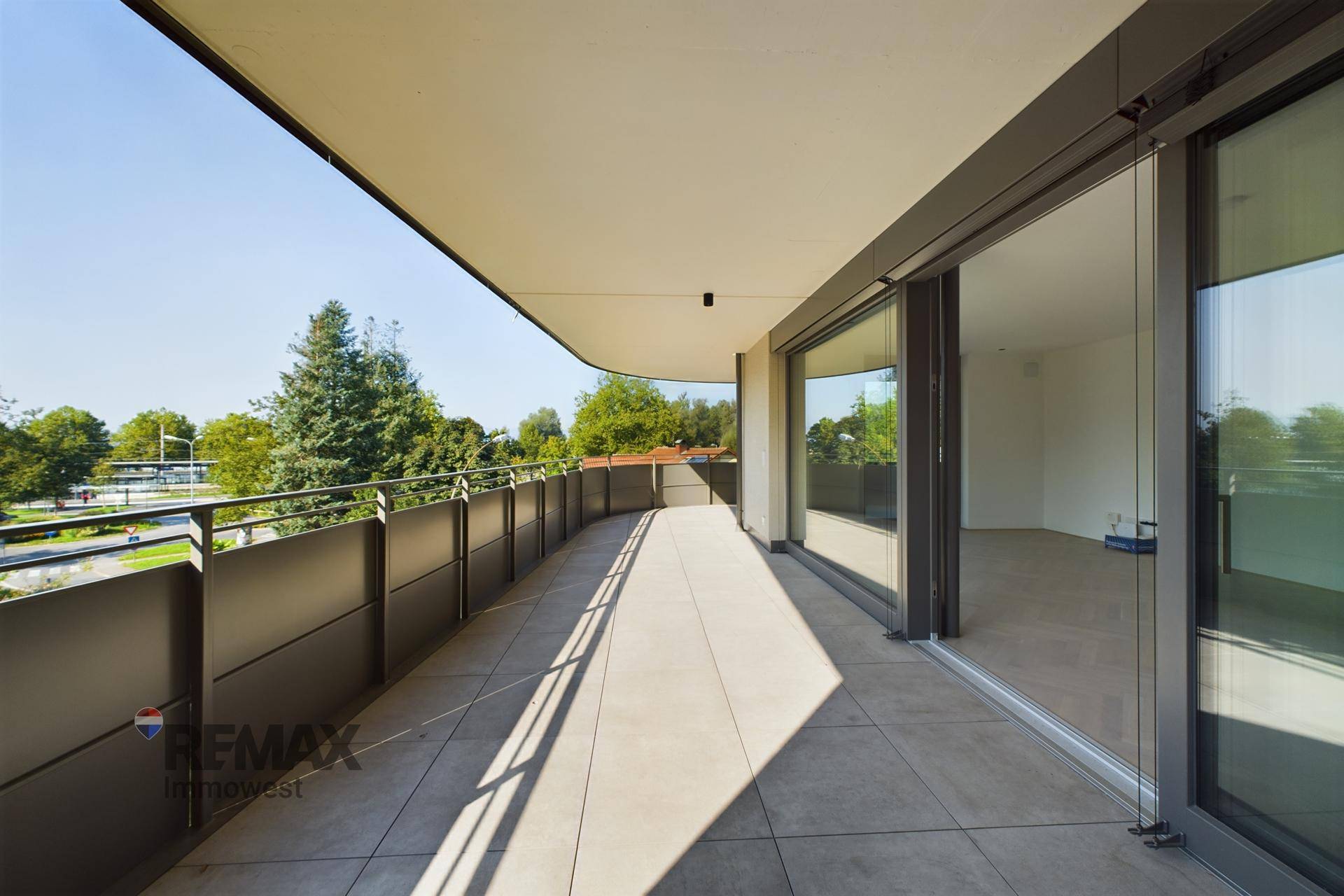 Breiter Balkon mit Fliesenboden und großen Glasschiebetüren, die viel Licht in den Innenraum lassen.