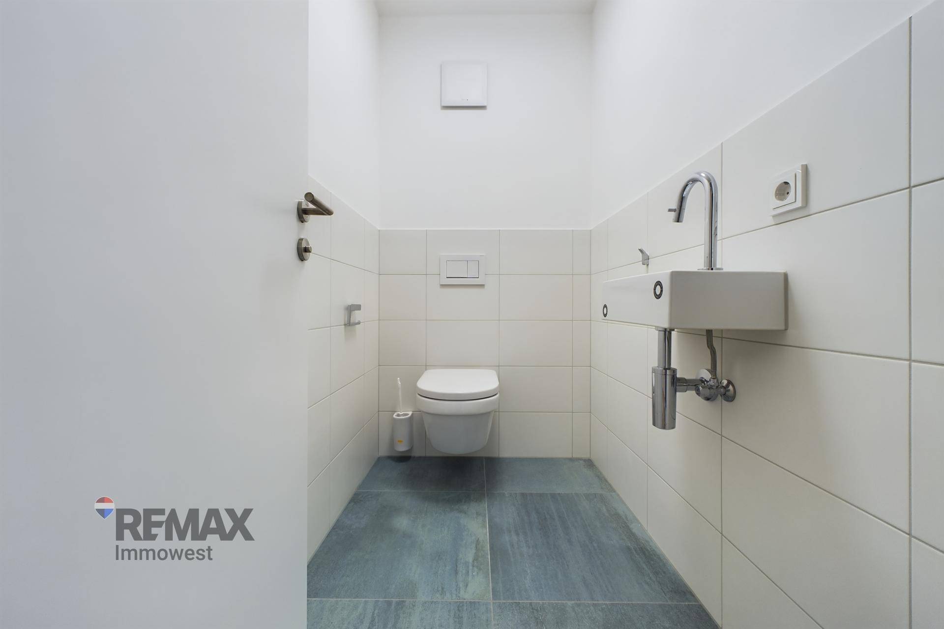 Modernes Gäste-WC mit weißen und grauen Fliesen, wandhängendem WC und kleinem Waschbecken.