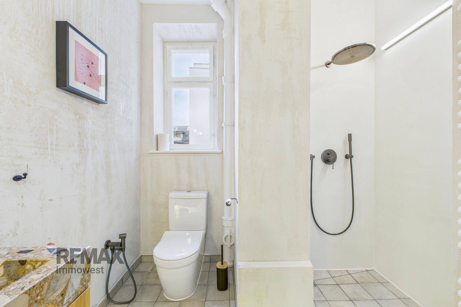 Badezimmer mit moderner Dusche, Toilette und Fenster, das viel Tageslicht hereinlässt.