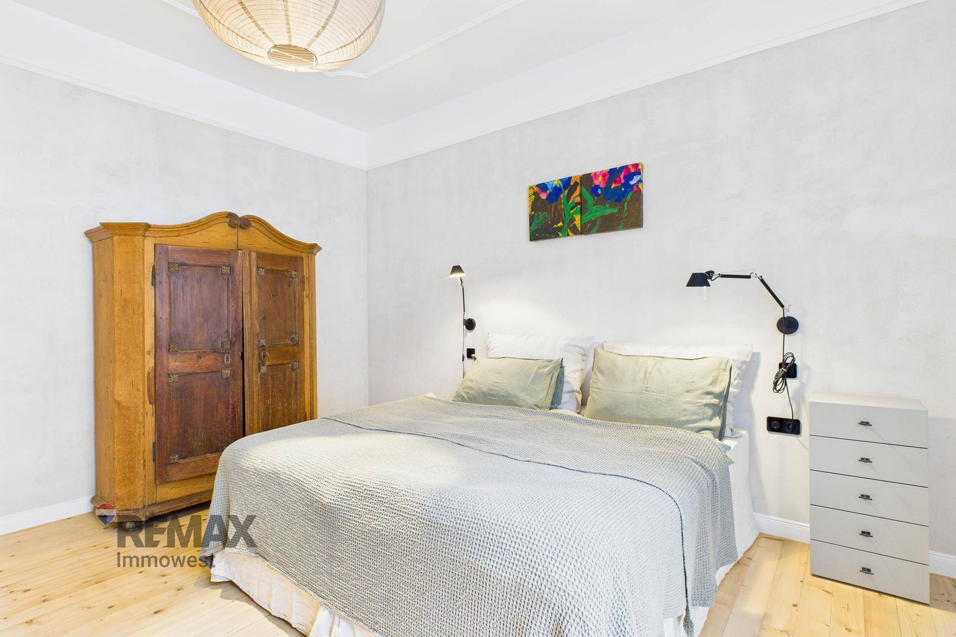 Schlafzimmer mit Holzboden, antikem Kleiderschrank und modernem Doppelbett.