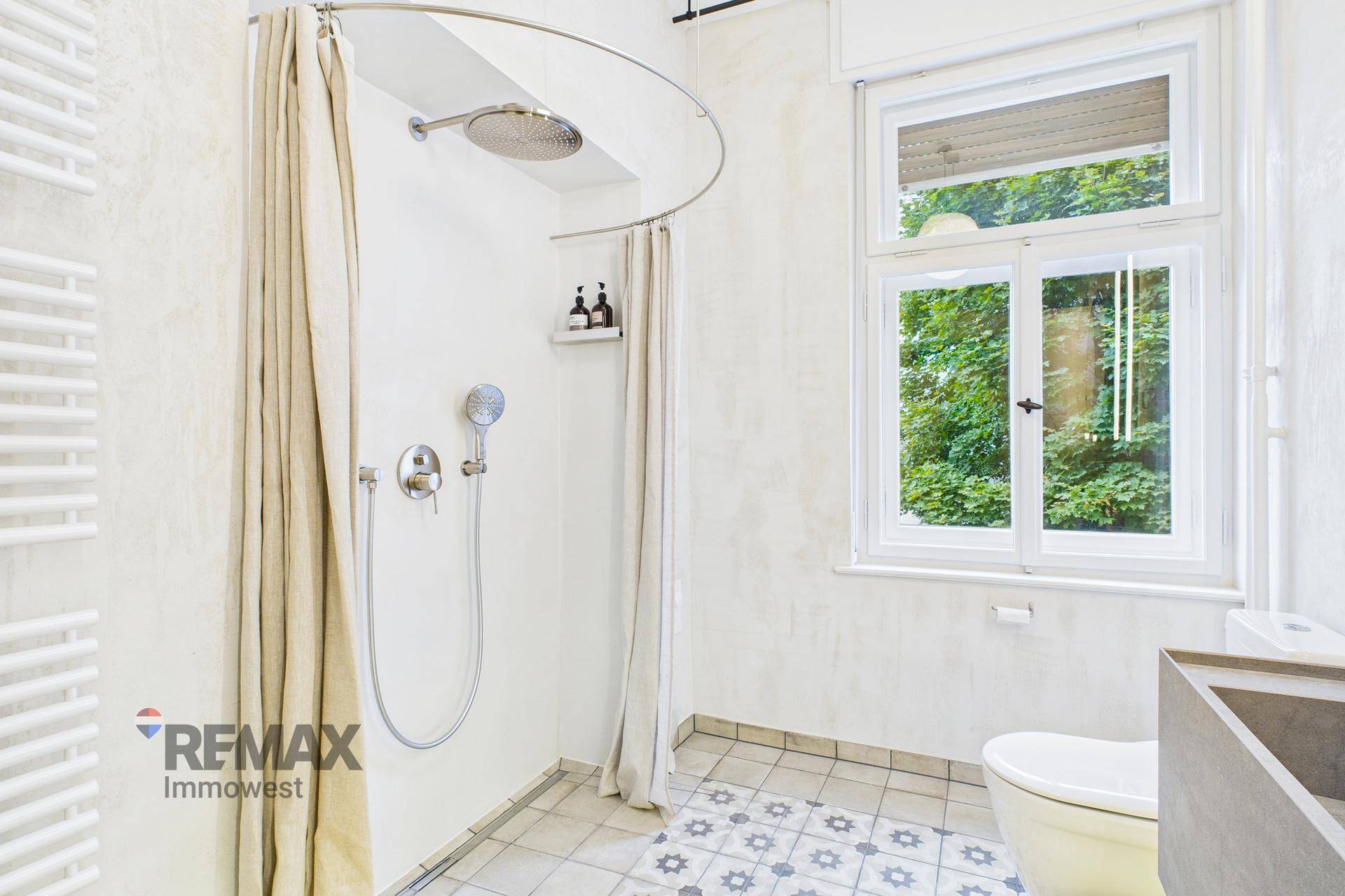 Geräumige Dusche mit Regenduschkopf und Fenster mit Blick ins Grüne.